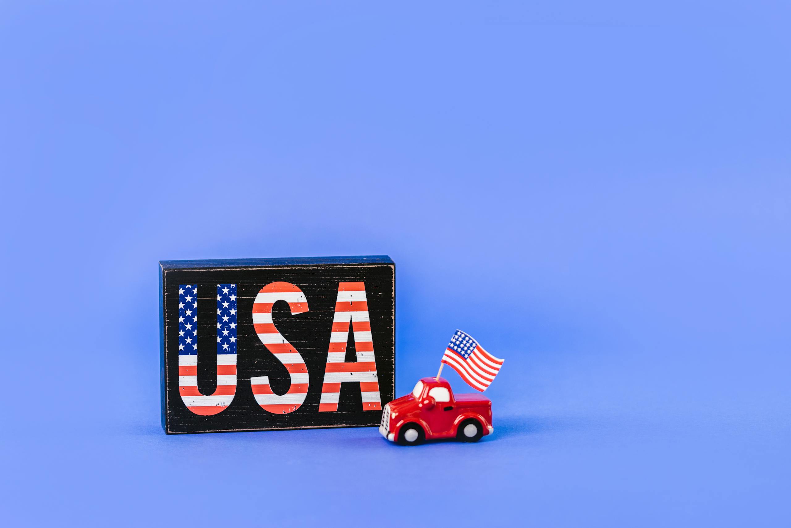 Patriotic USA sign with miniature car and American flag on blue background.