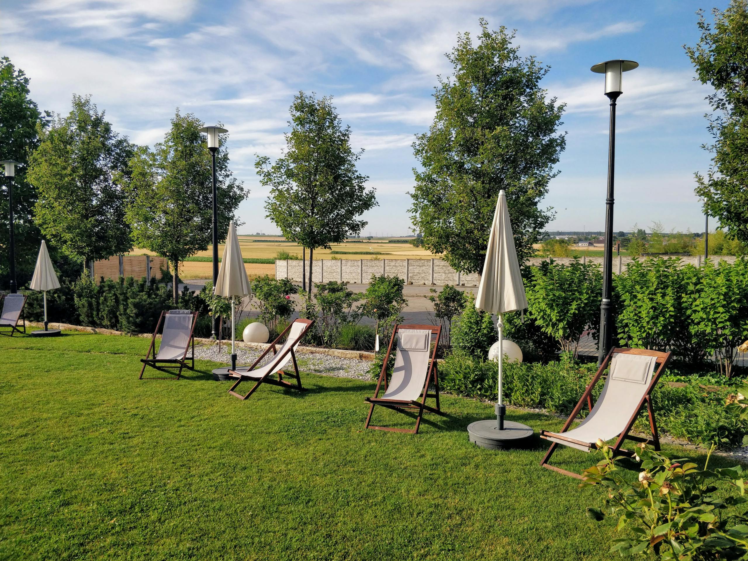 Peaceful outdoor garden setting with empty loungers and umbrellas surrounded by greenery.