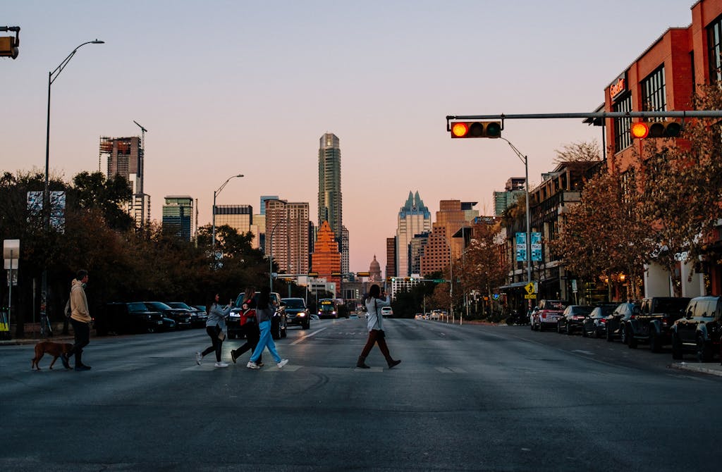 People crossing a city street in Austin, Texas at sunset with the skyline in the background.