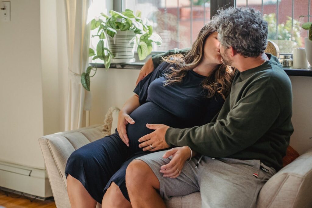 /couple-expecting-baby-sitting-on-daybed-and-kissing
