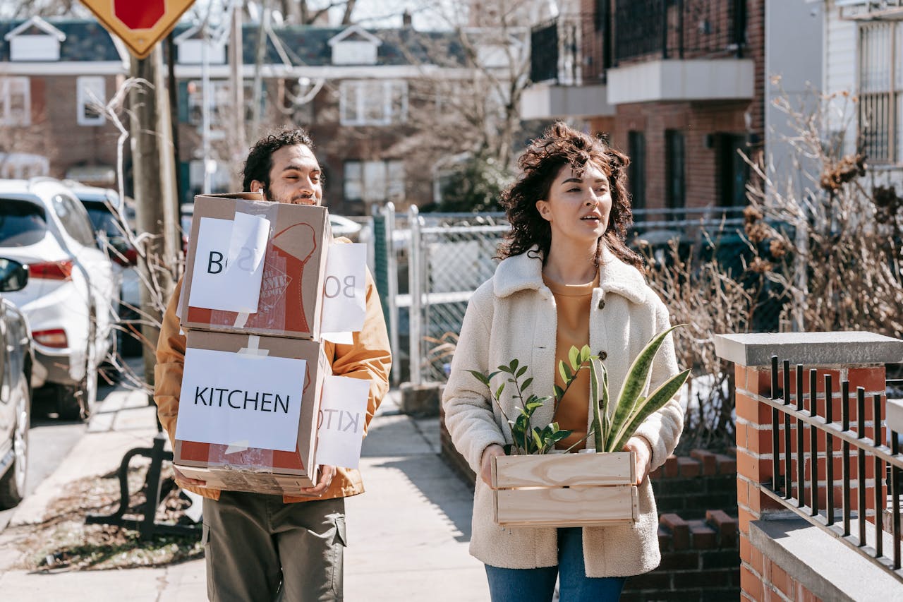 a-couple-moving-out-carrying-boxes-and-plants-