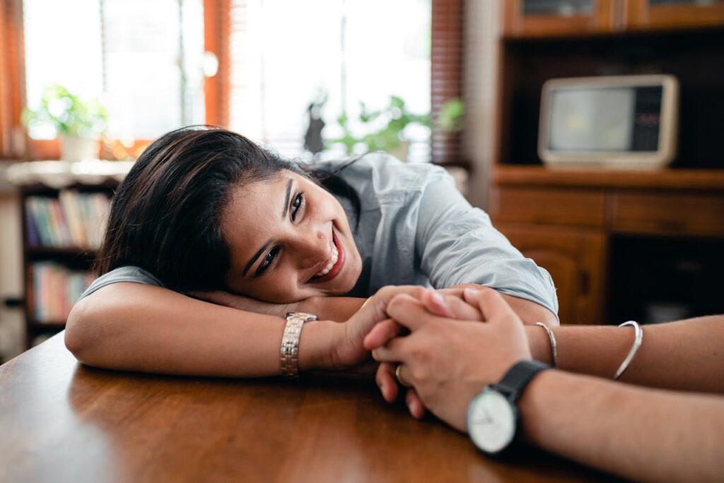 ethnic-woman-sitting-at-table-and-smiling-while-holding-hand-of-husband