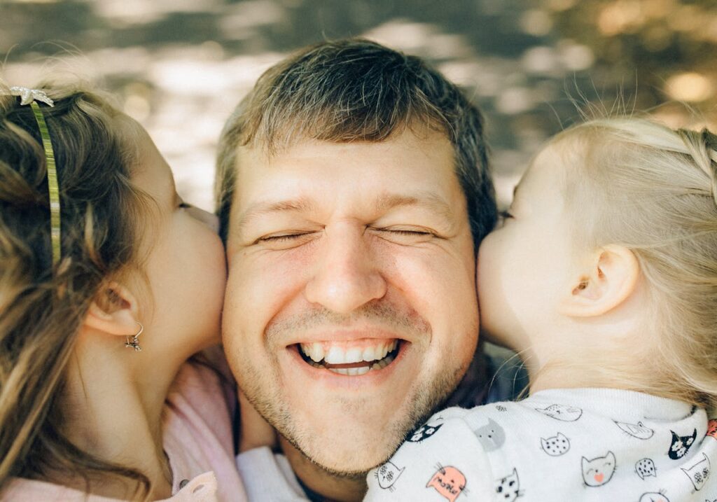 a-man-being-kissed-by-his-daughters-