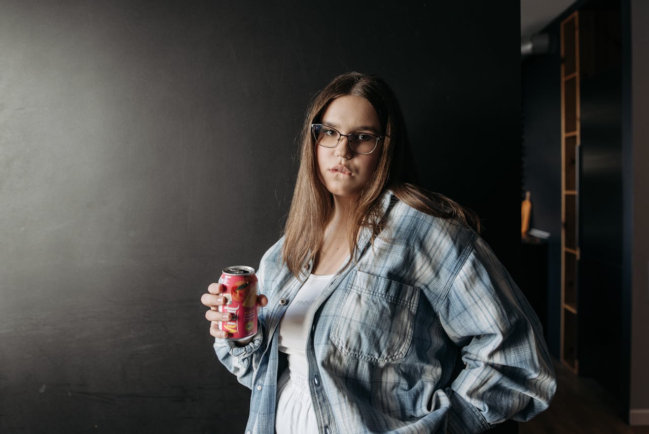 a-woman-in-plaid-long-sleeves-holding-a-can-of-soda-while-looking-at-the-camera-