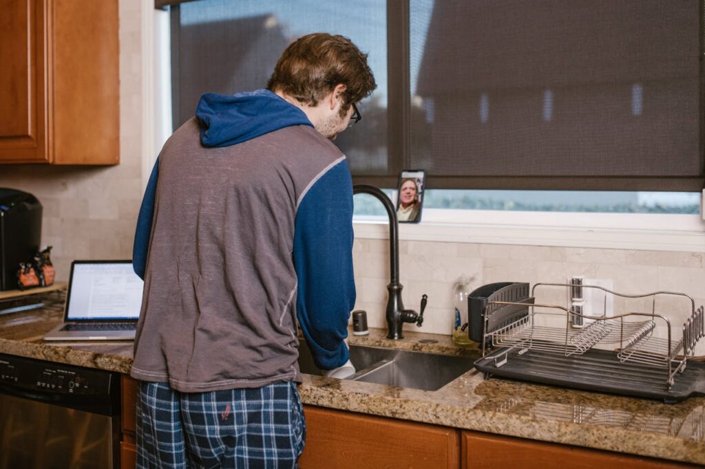 a-man-standing-near-the-kitchen-sink-while-doing-video-call-on-his-mobile-phone-