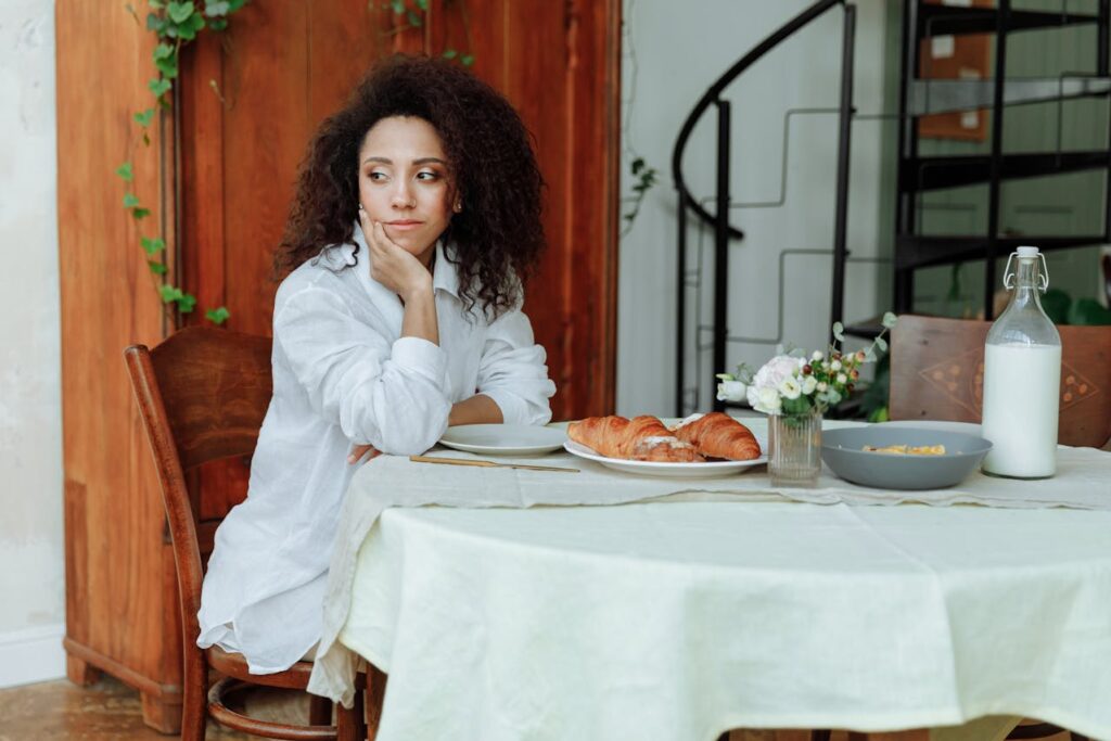 /woman-with-curly-hair-sitting-near-a-plate-of-croissants