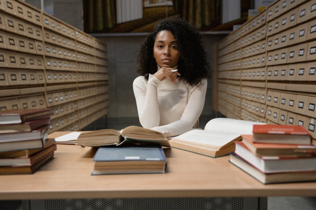 a-woman-with-curly-hair-sitting-on-a-table-with-stacks-of-books