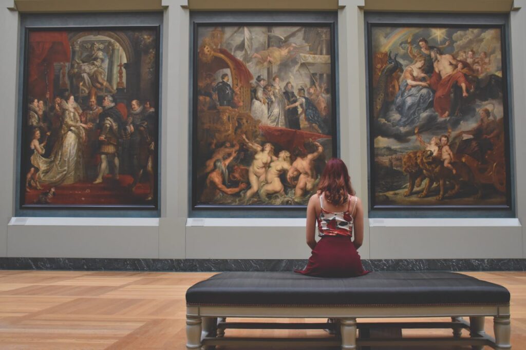 /woman-sitting-on-ottoman-in-front-of-three-paintings