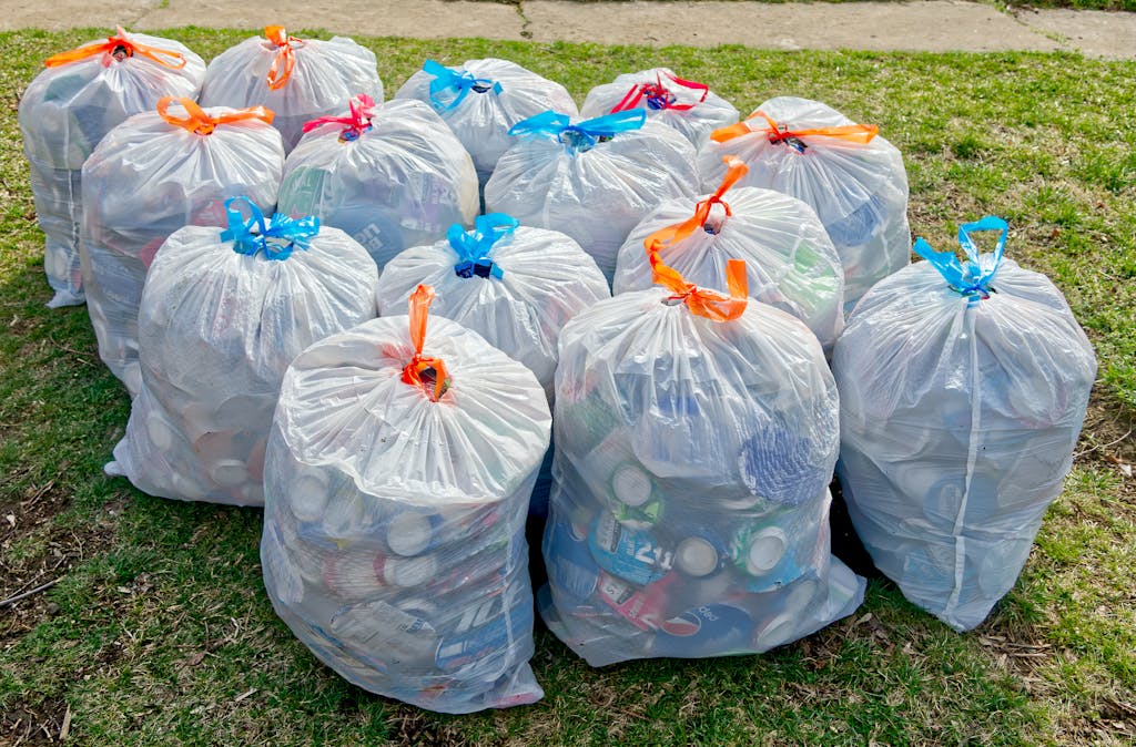 Plastic trash bags filled with recyclable materials on grass, raising recycling awareness.