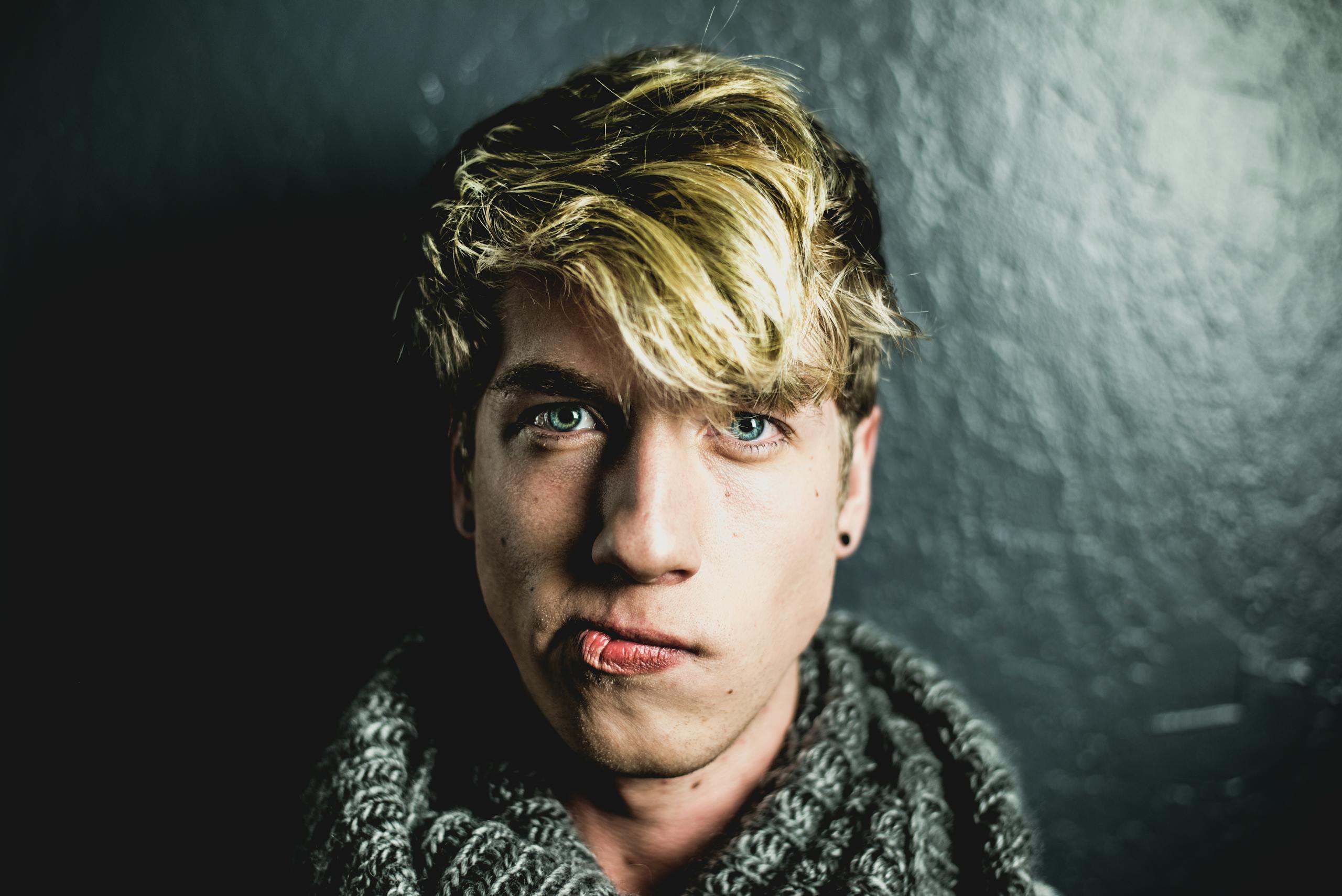 Portrait of a young man with blonde hair wearing a scarf against a dark background.