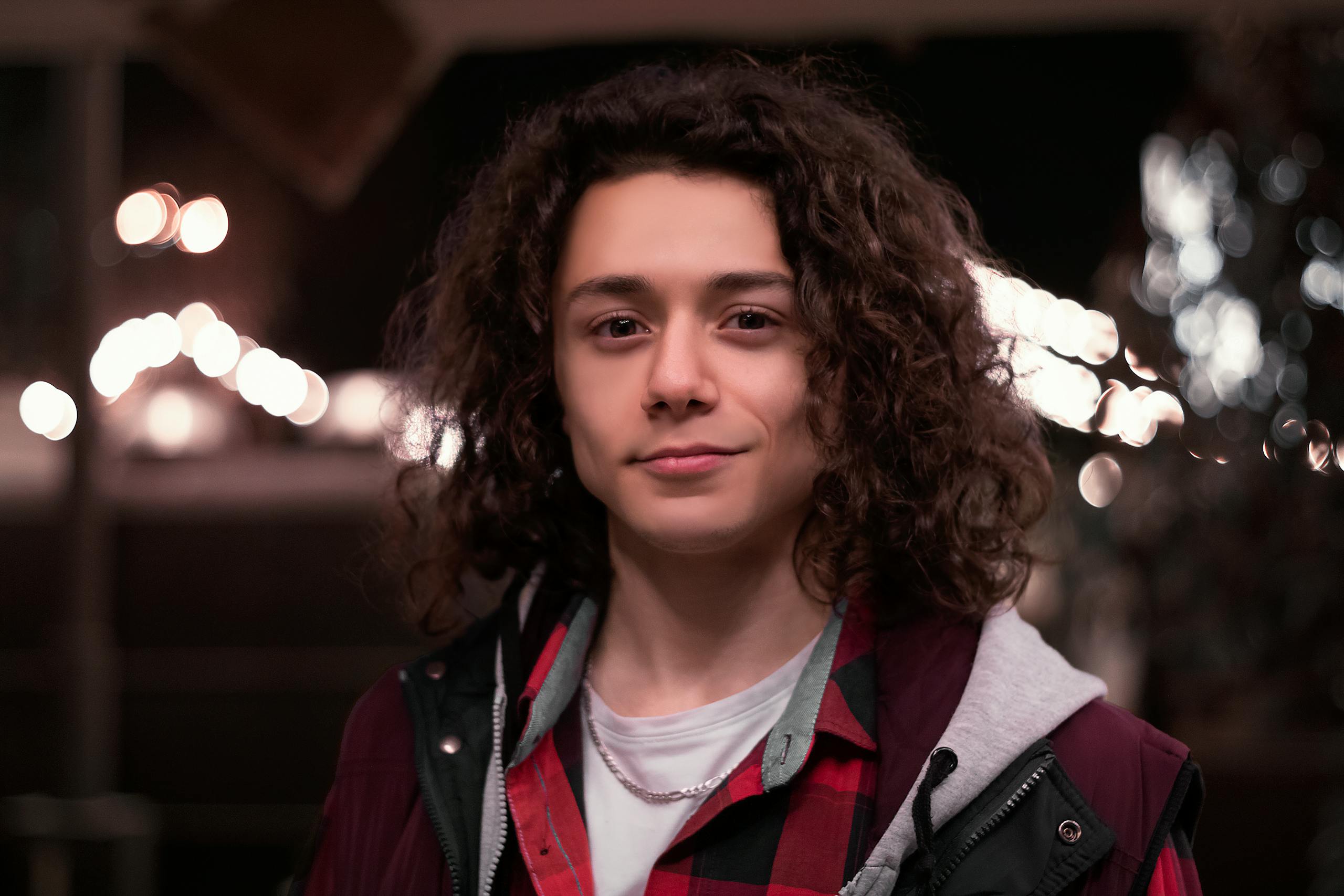Portrait of a young man with curly hair wearing a checkered shirt at night in Tehran, Iran.