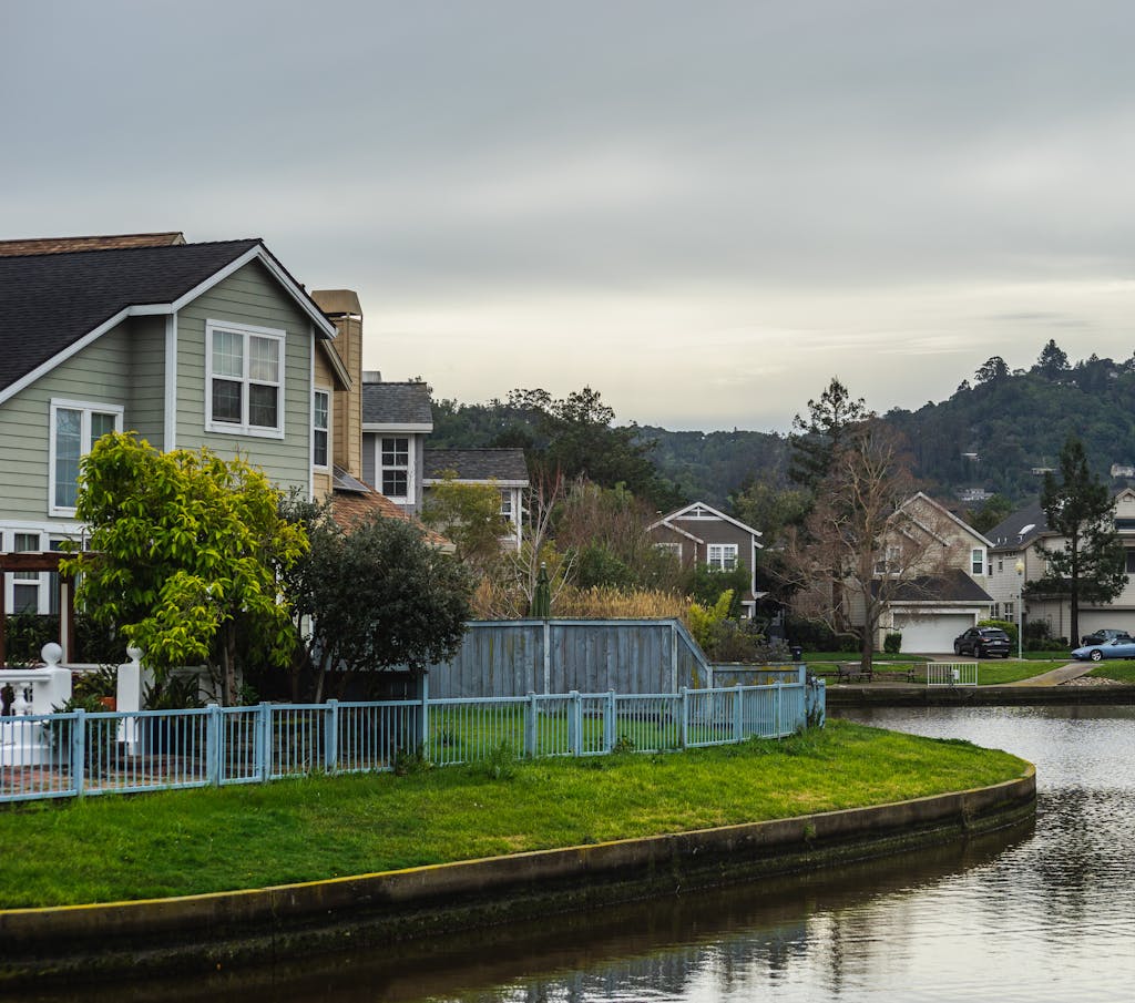 Quaint residential suburb with homes by a serene canal under a cloudy summer sky.
