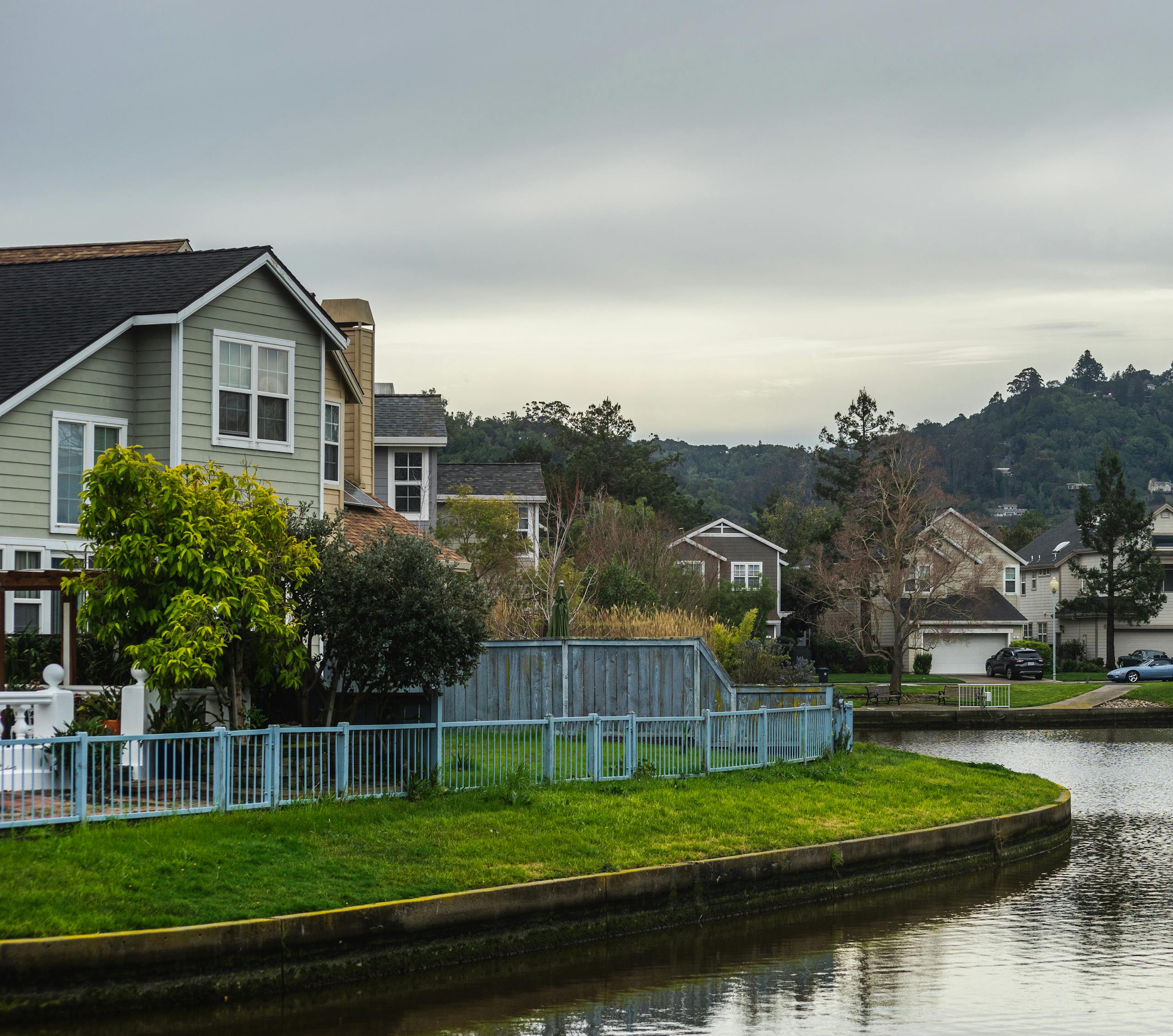 Quaint residential suburb with homes by a serene canal under a cloudy summer sky.
