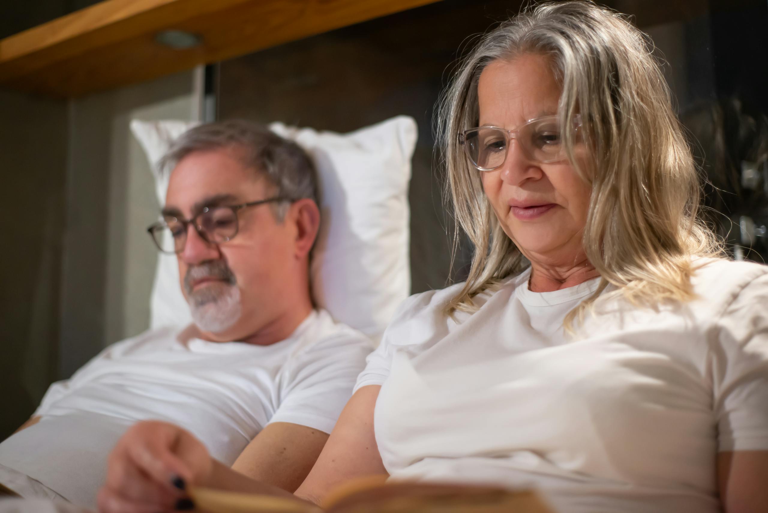 Relaxed elderly couple reading together in bed, enjoying leisure time and companionship.