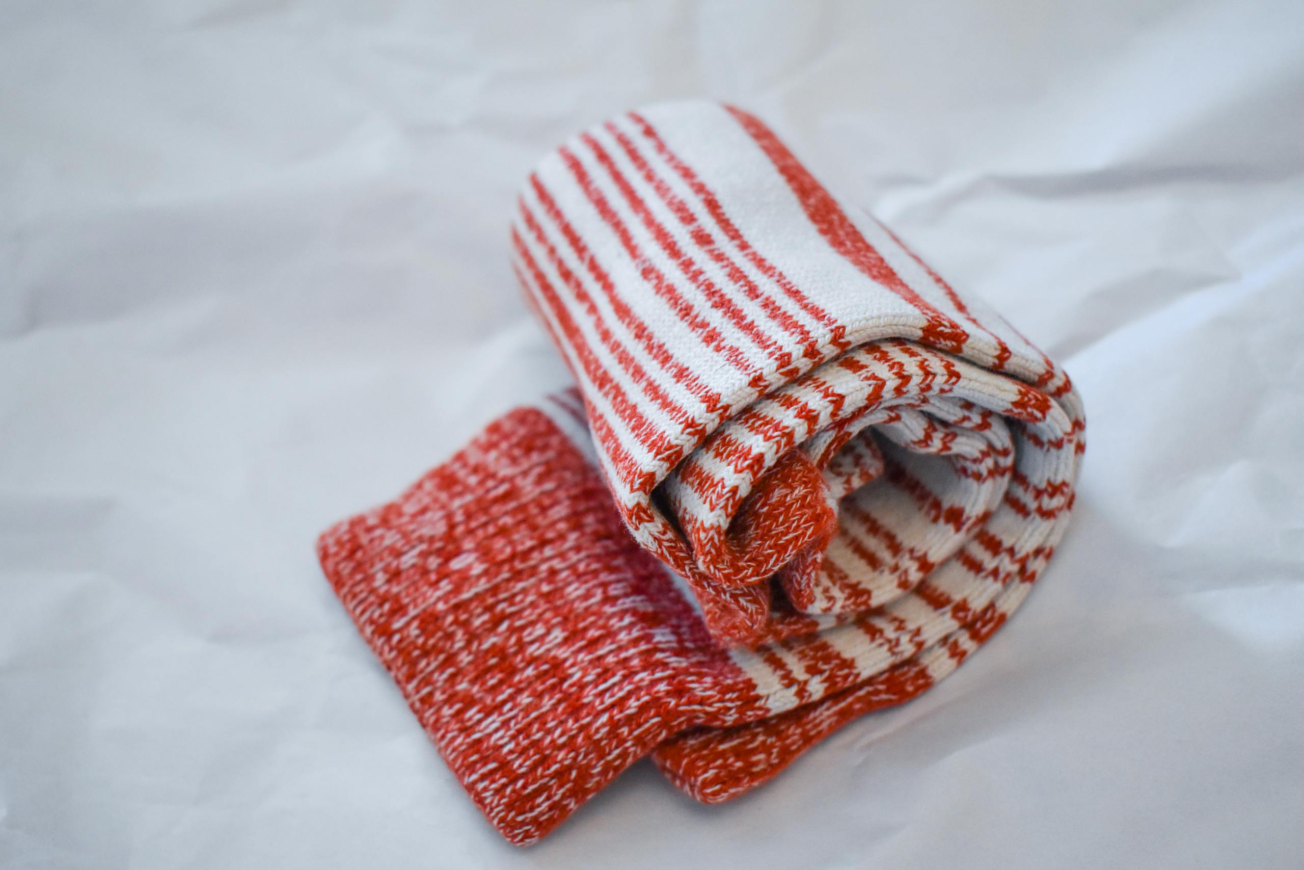 Rolled red and white striped winter socks on a minimal white surface, perfect for comfort and warmth.
