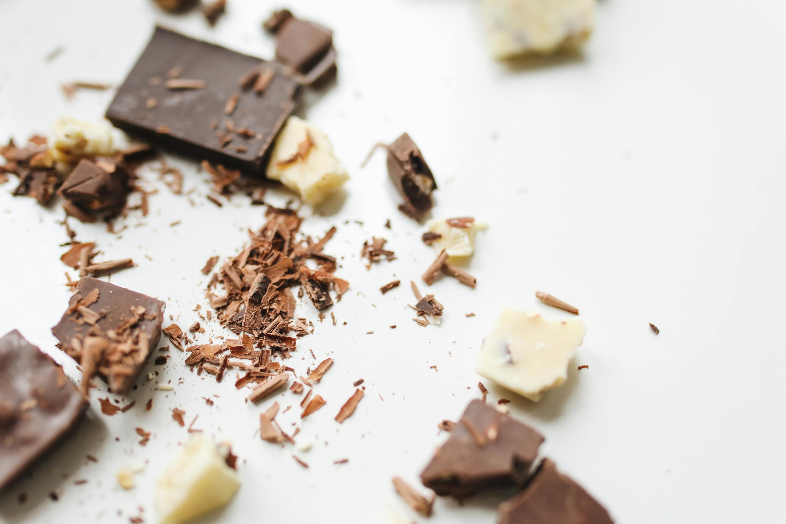 Scattered chocolate chunks and shavings on a white background, showcasing dessert ingredients.