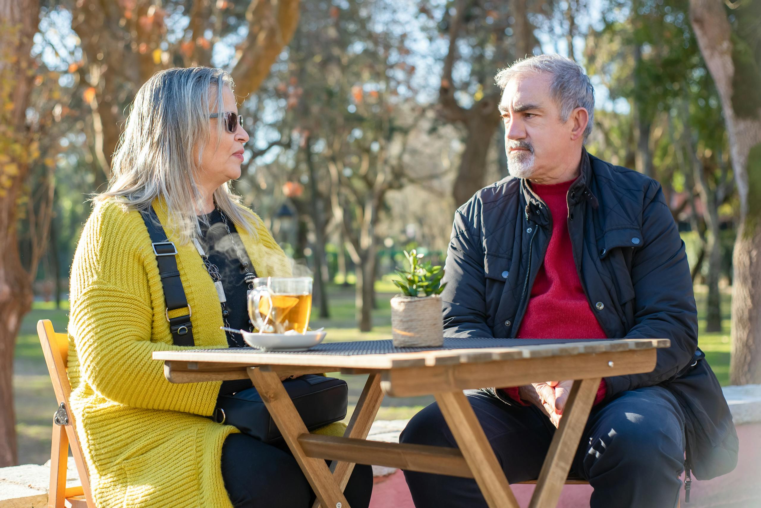Senior man and woman enjoy a tea conversation in a sunny Portuguese park.
