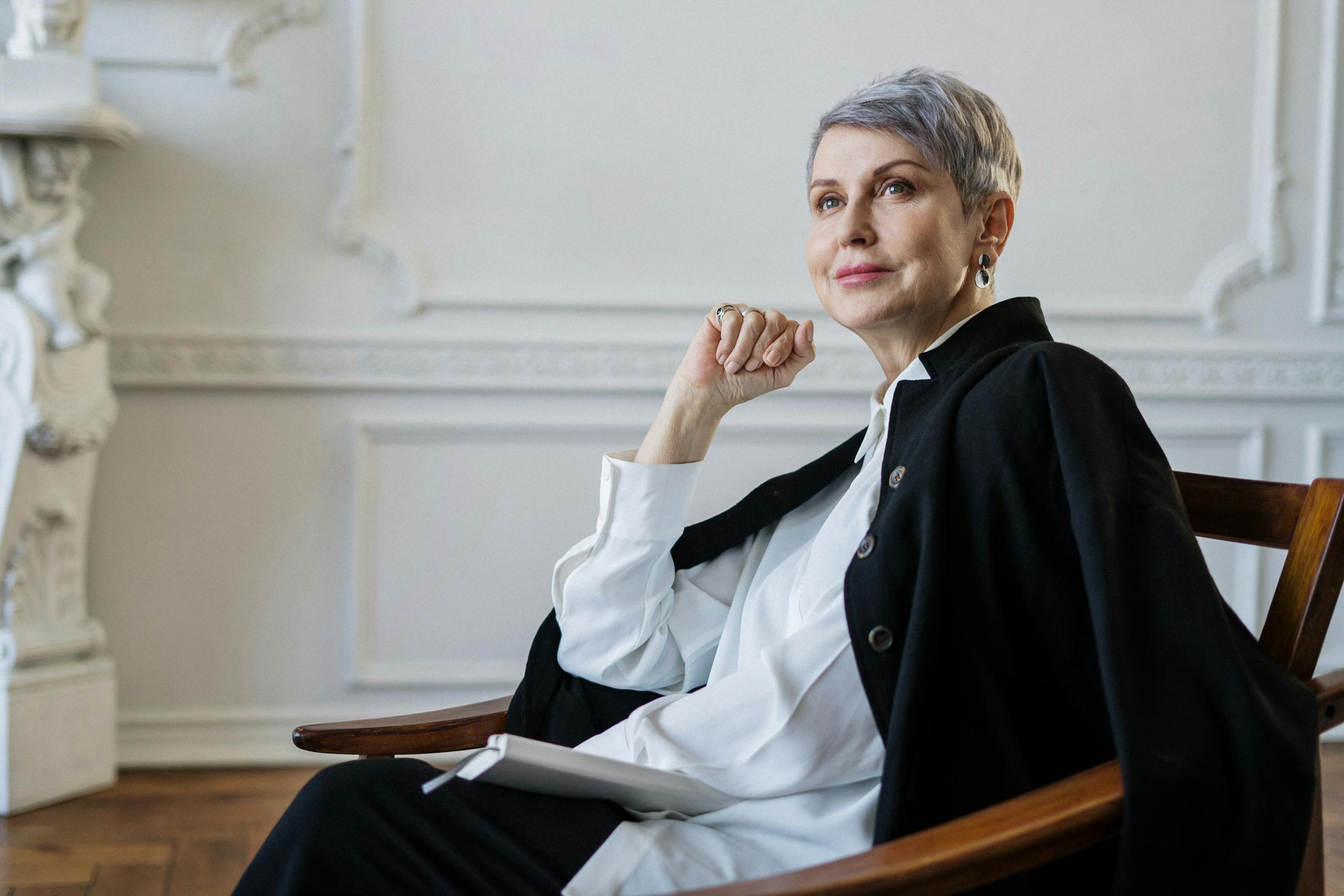 Senior woman with short hair seated indoors, exuding confidence and elegance in a classic setting.