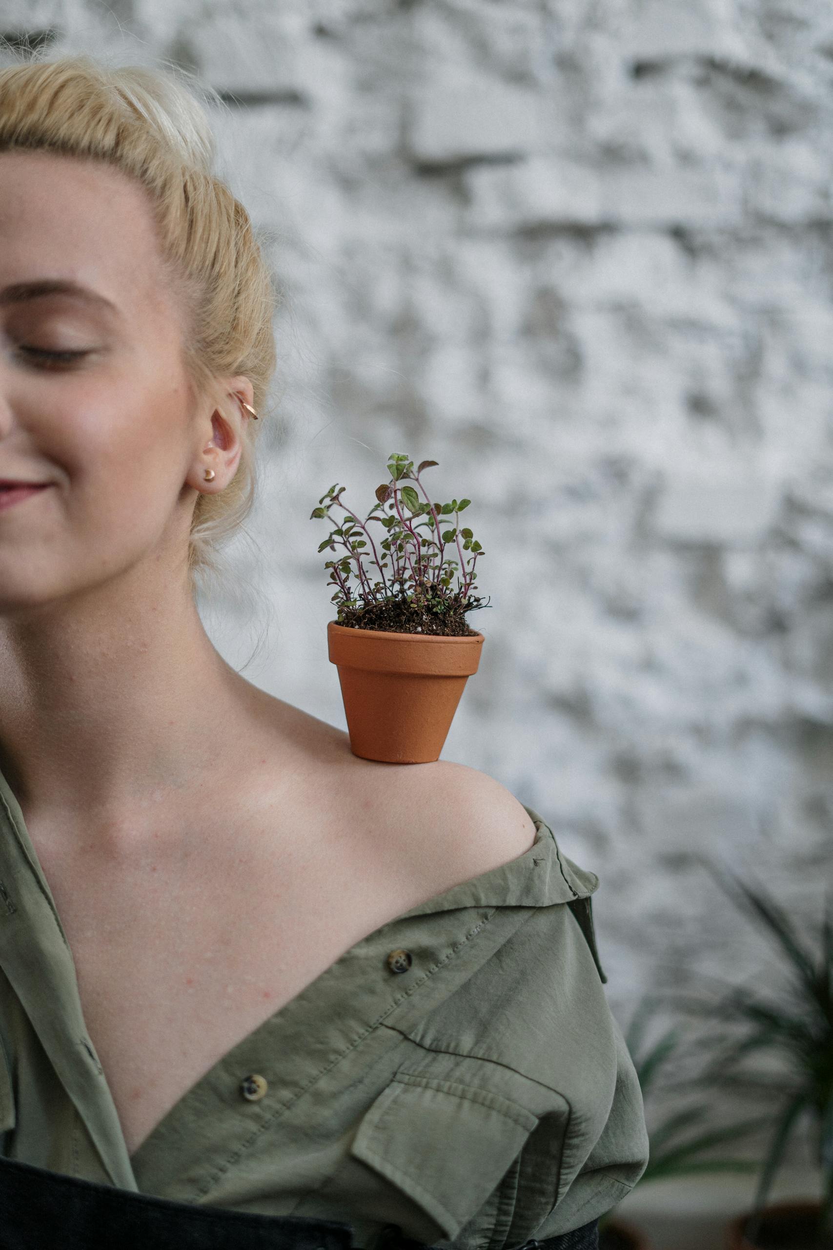 Serene woman balancing a potted plant on her shoulder, showcasing home gardening creativity.