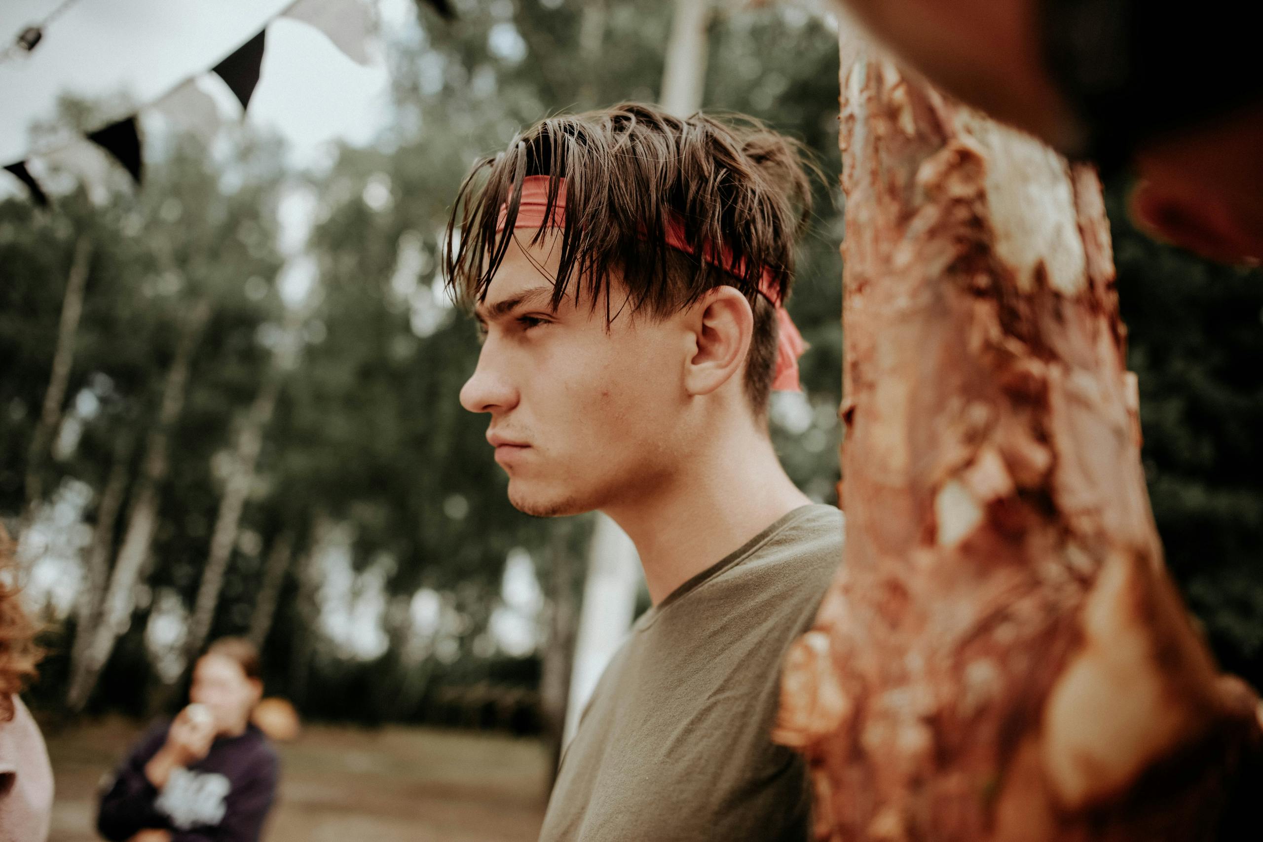 Side profile of a young man in a bandana outdoors, focused and serious.