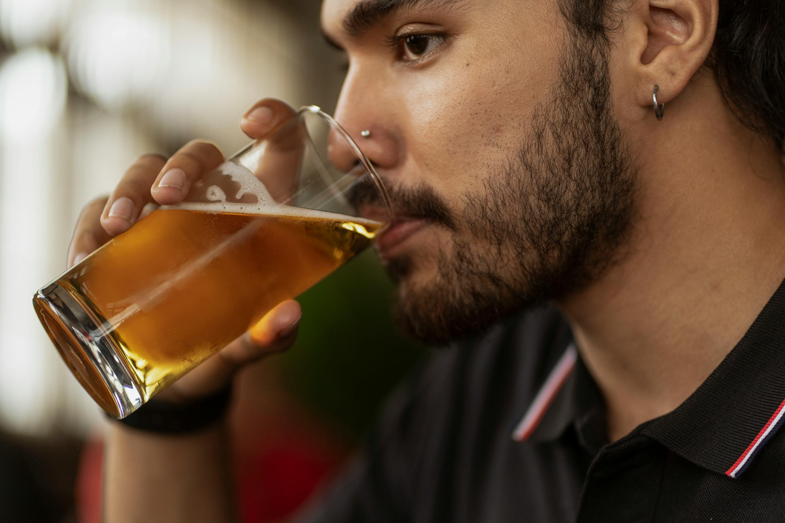 Side view of a bearded man sipping beer from a glass at a pub.