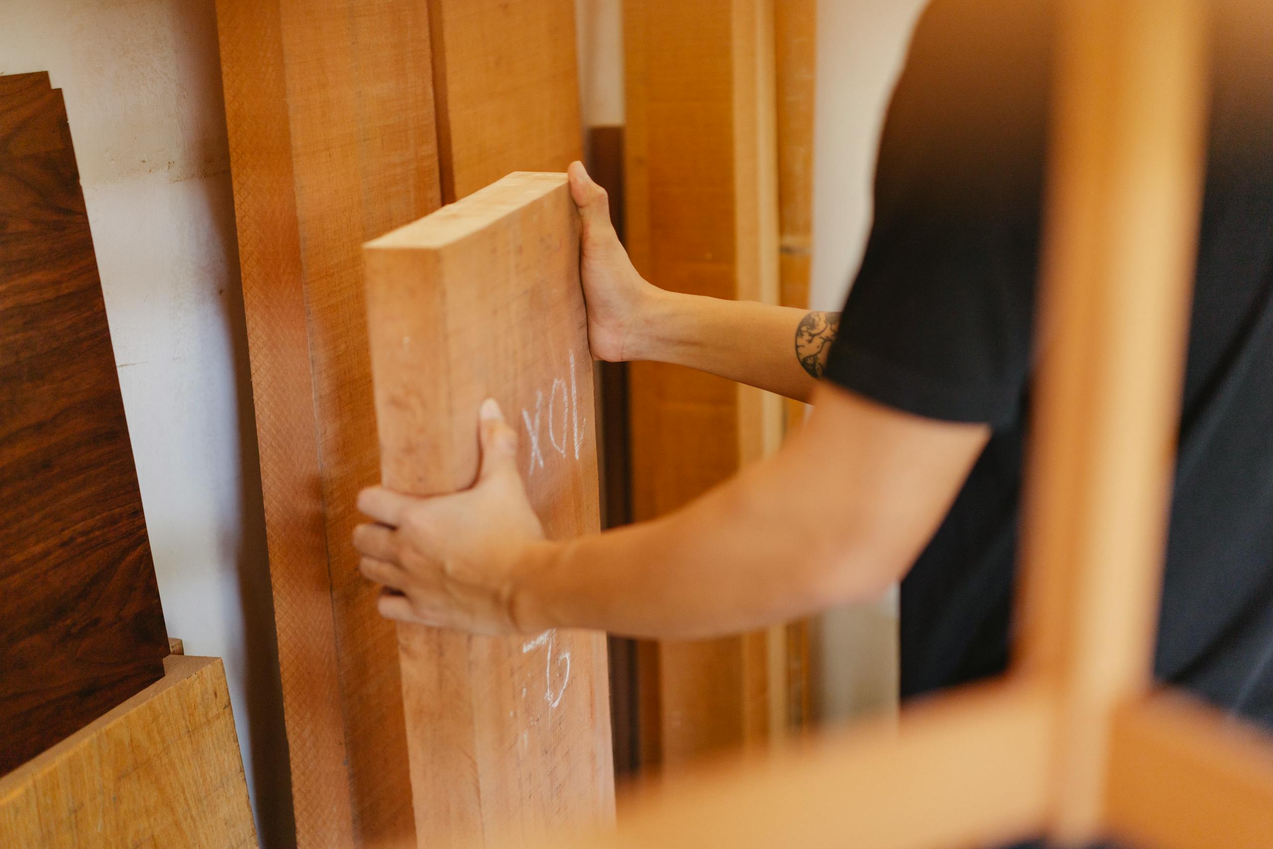 Side view of crop anonymous joiner choosing wooden plank from assortment of timber in workshop