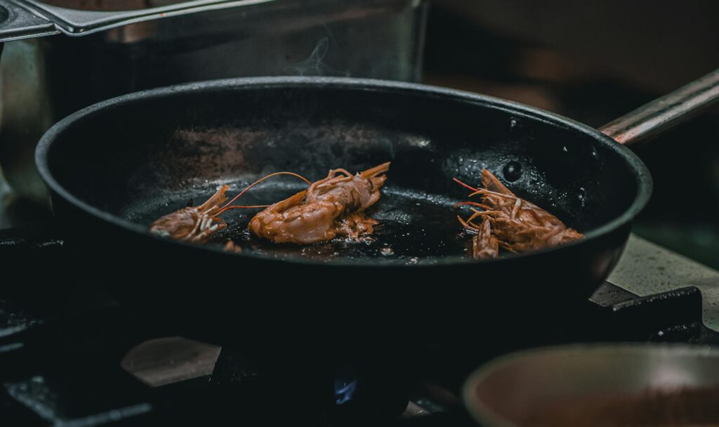 Sizzling prawns being cooked in a frying pan in a professional kitchen setting.