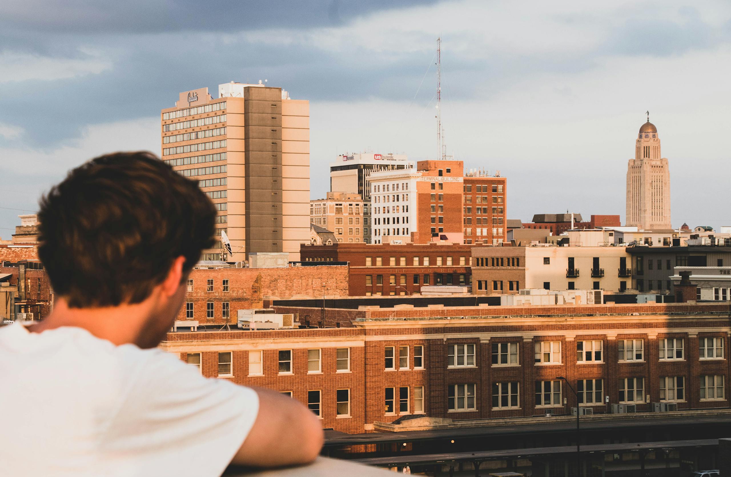Skyline of Lincoln, NE with a man observing at sunset, featuring the State Capitol.