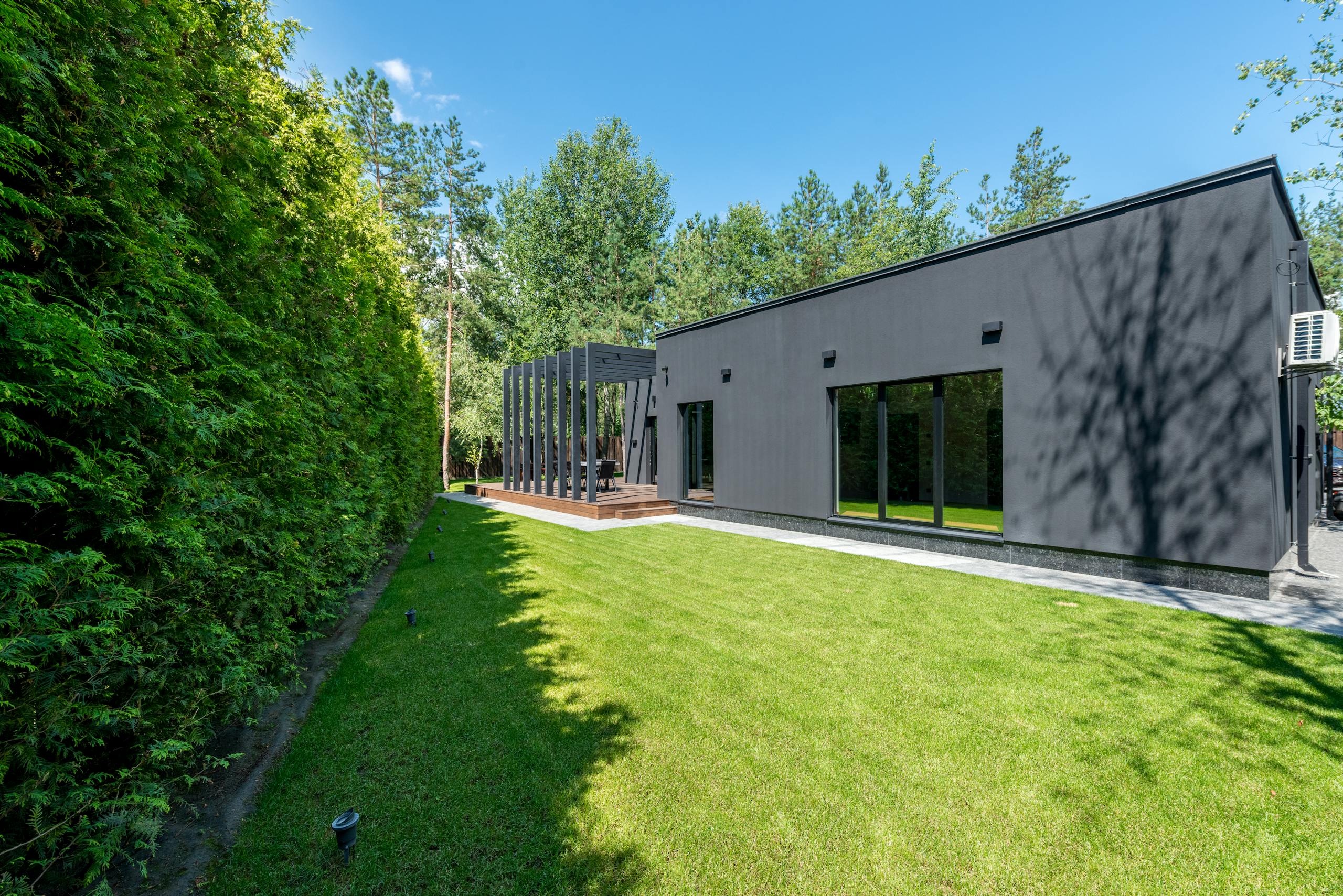 Sleek black modern house with large windows and vibrant green lawn surrounded by dense trees.
