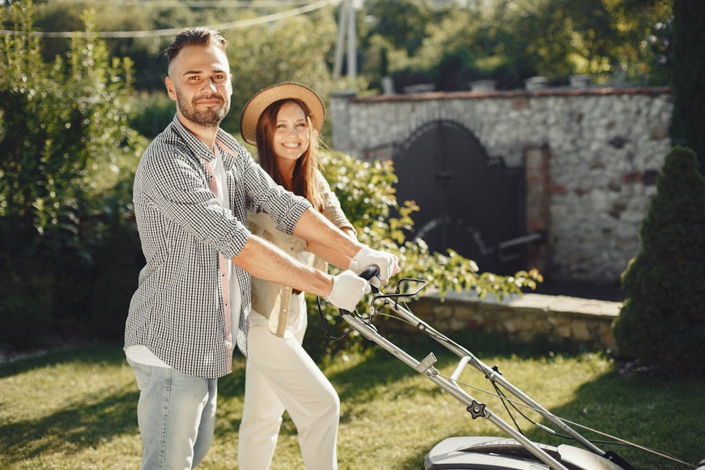 Smiling couple enjoys gardening together, using lawn mower in sunny outdoor garden.