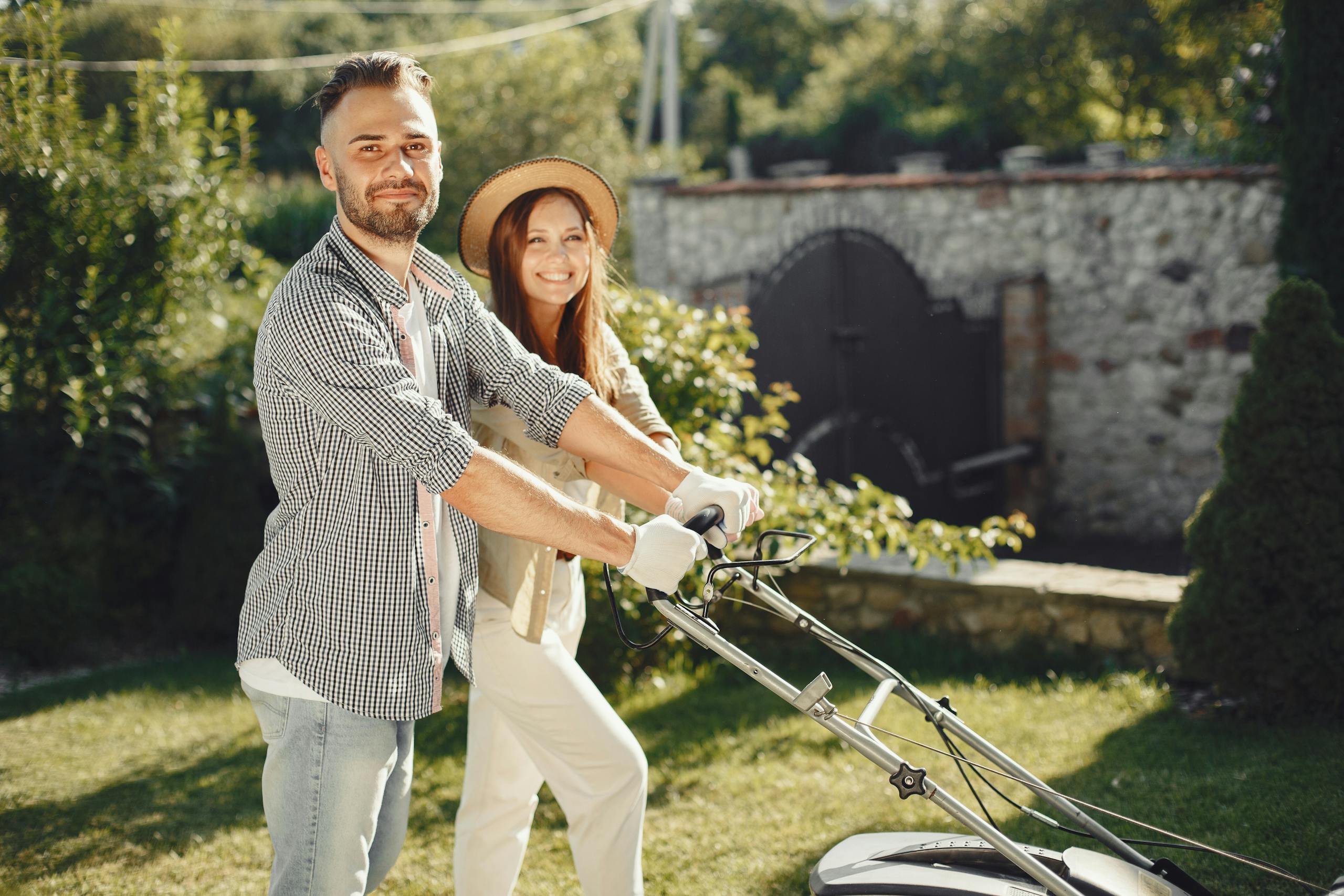 Smiling couple enjoys gardening together, using lawn mower in sunny outdoor garden.
