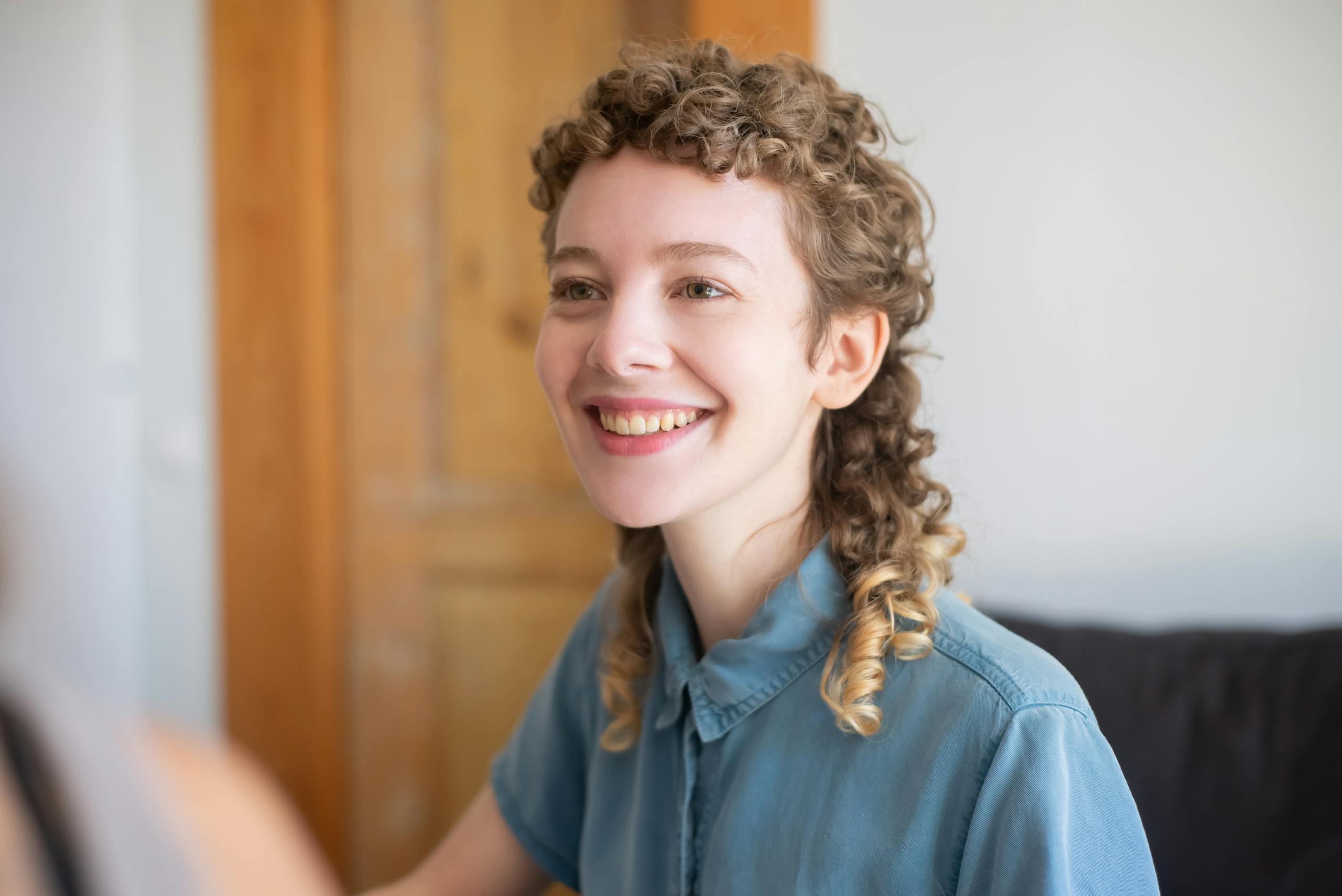 Smiling young woman with curly hair, indoors in Portugal, exuding warmth and happiness.