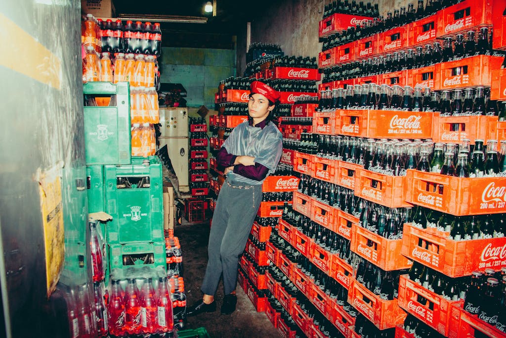 Stylish model posing among soda crates in a colorful warehouse.