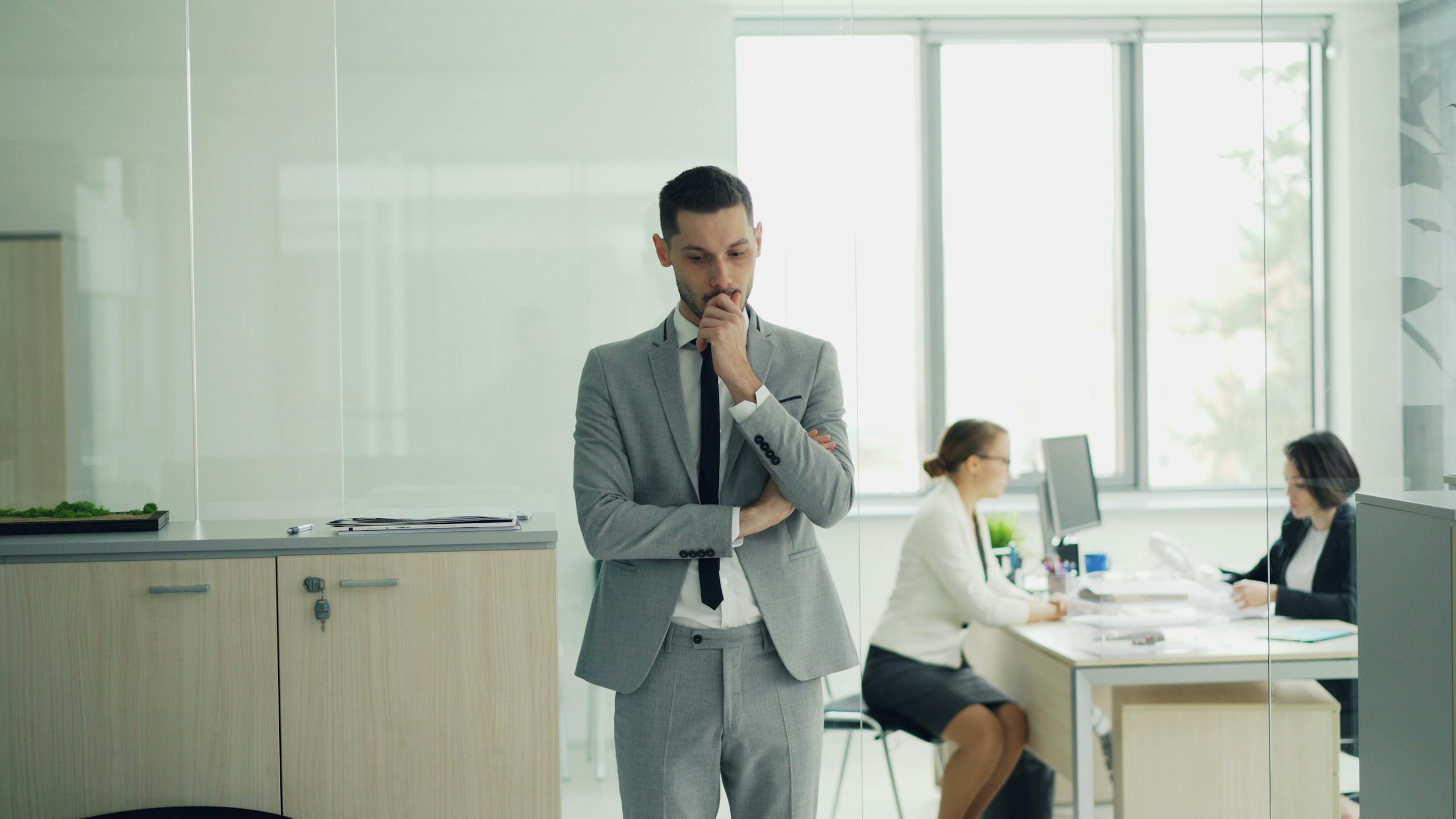 Thoughtful businessman in a modern office setting with colleagues working in the background.