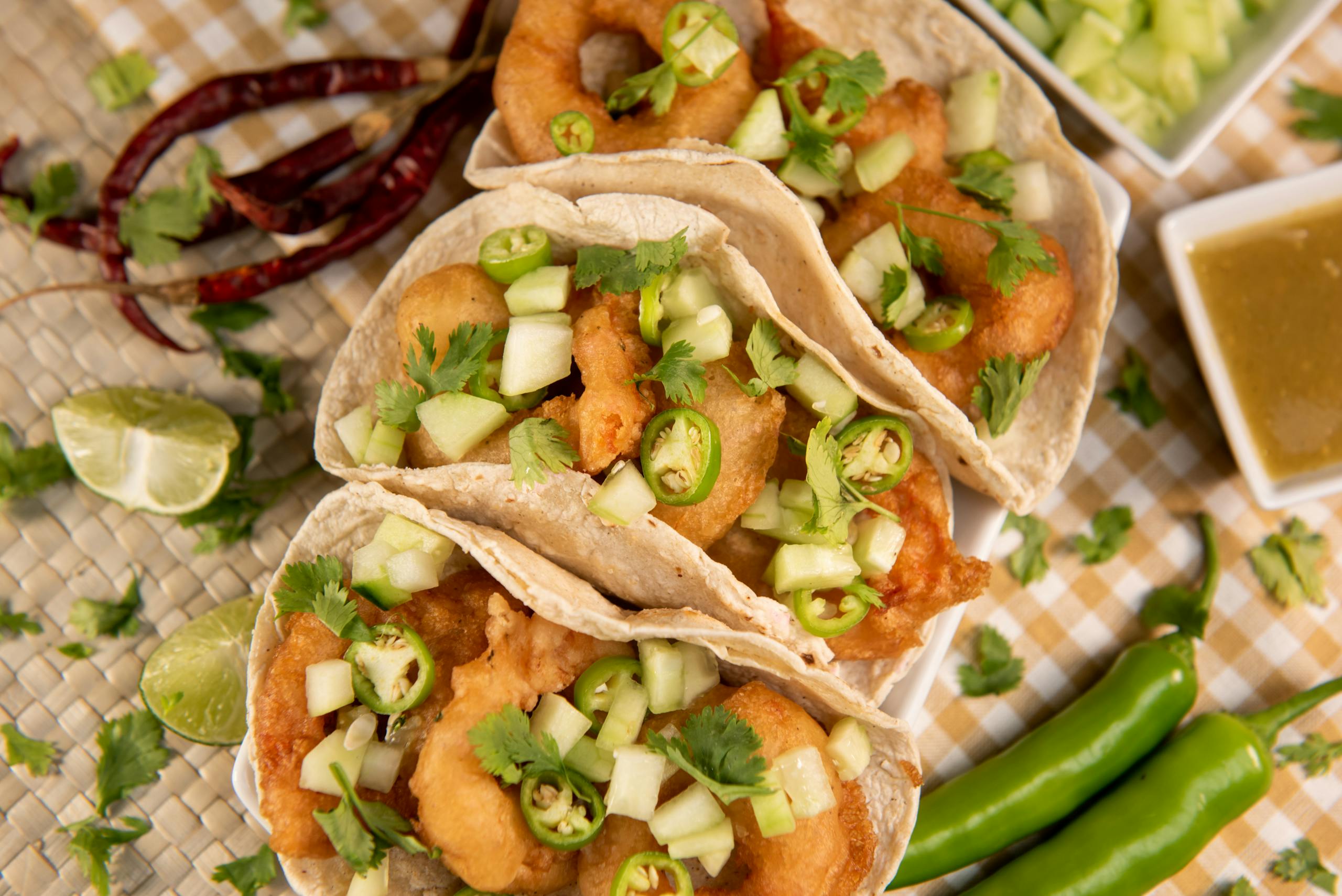 Three appetizing Mexican street tacos topped with fresh jalapeños, lime, and cilantro, served on a checkered tablecloth.