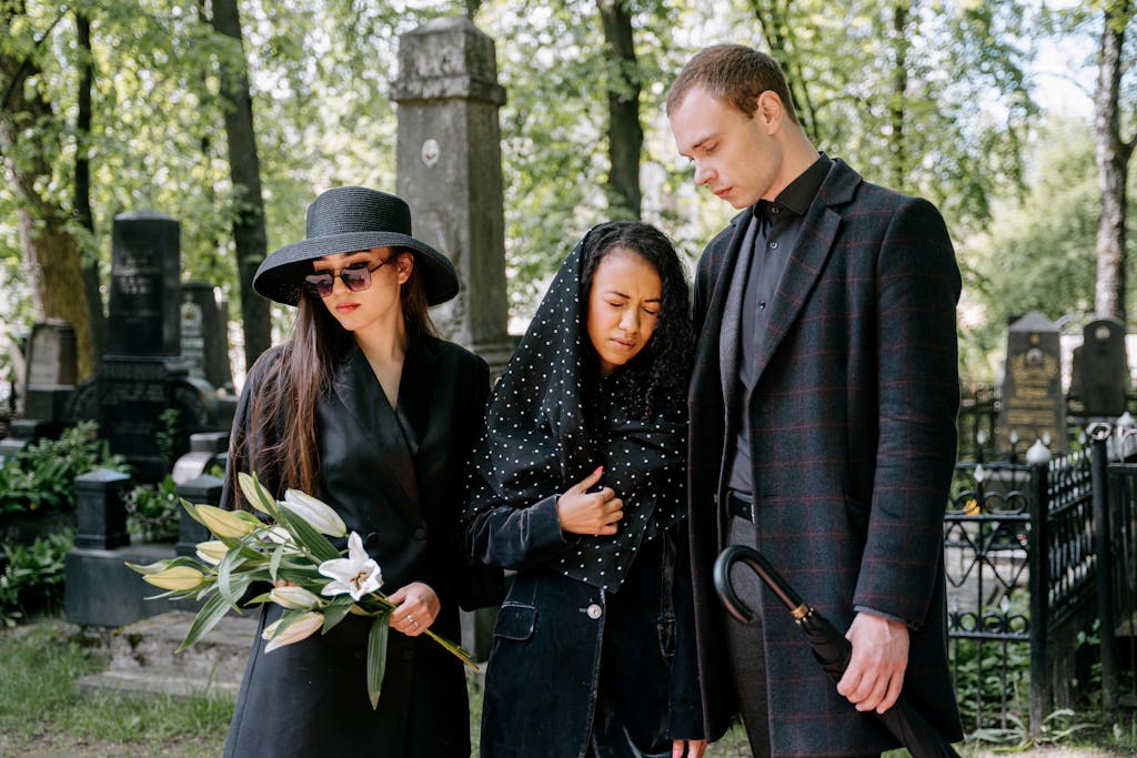 11 Signs You Shouldn’t Ignore, Unless You’re Ready for Things to Get Worse 5 Three mourners in a cemetery, expressing grief amidst tombstones and greenery.