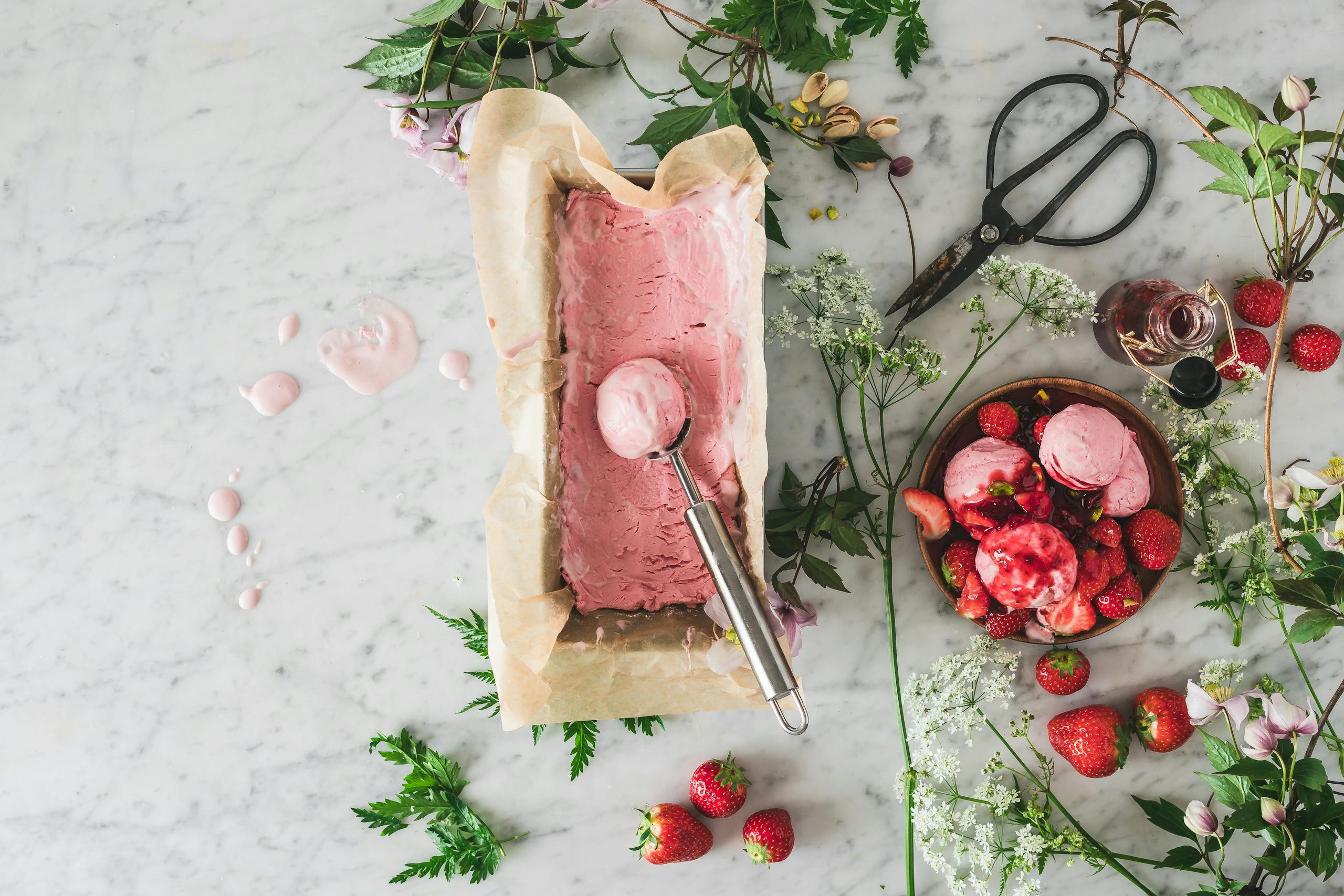 Top-down view of homemade strawberry ice cream with fresh berries and flowers in a rustic setting.