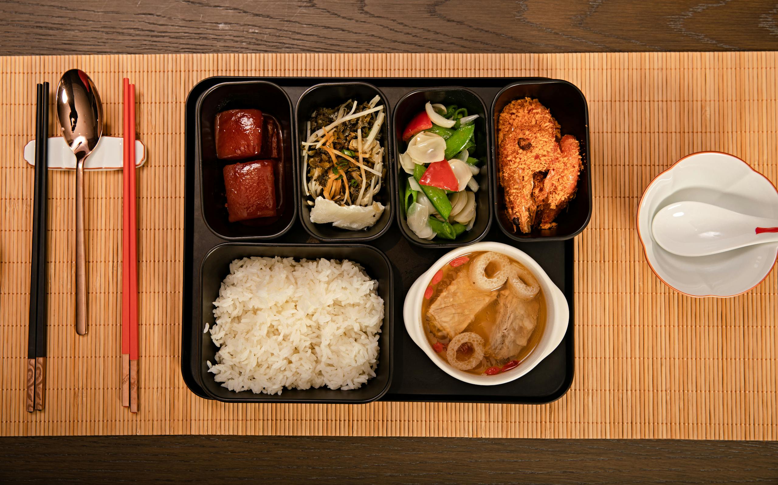 Top view of a traditional Asian bento box with diverse dishes and chopsticks on a bamboo mat.