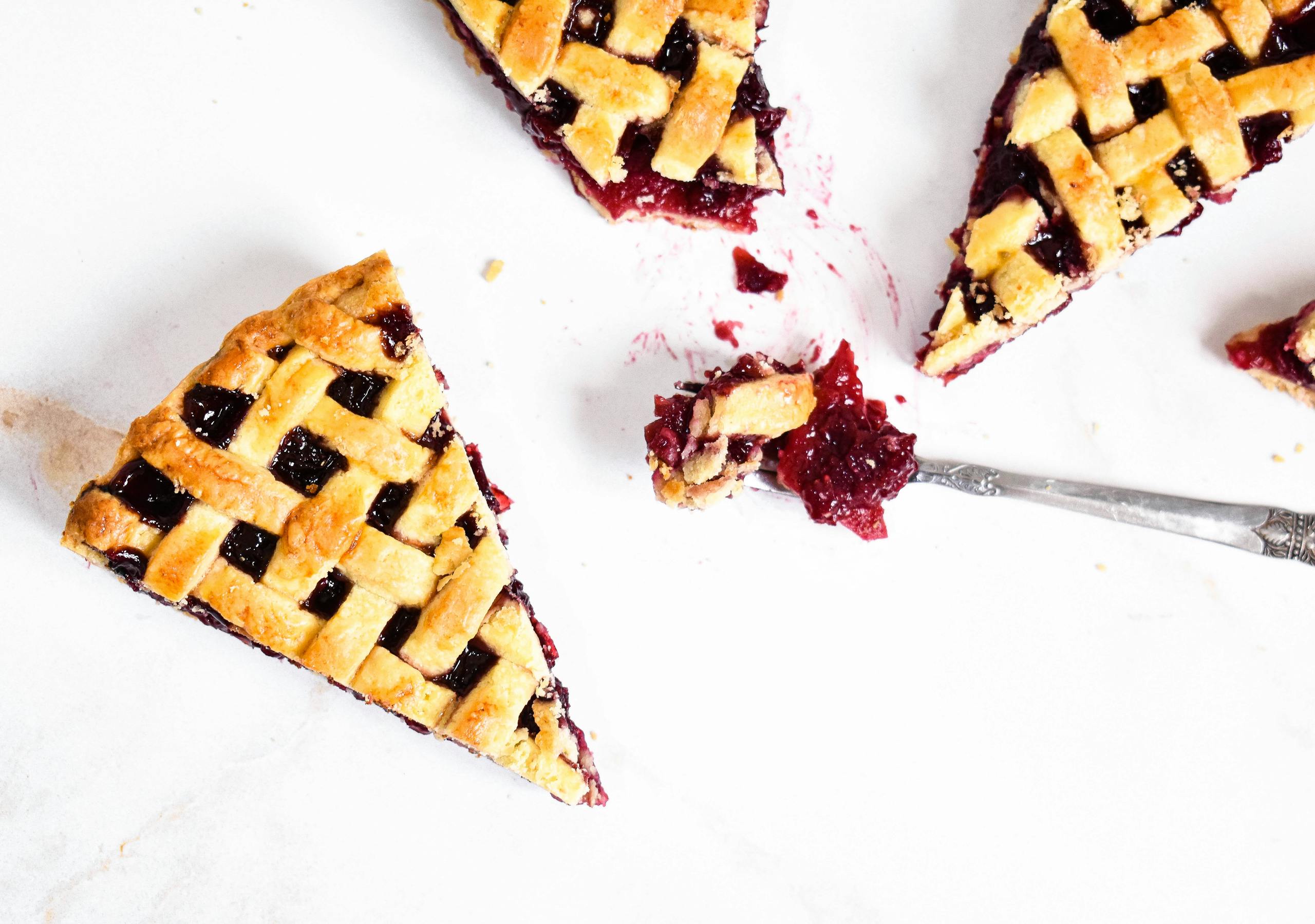 Top view of cherry pie slices with lattice crust on a white surface.