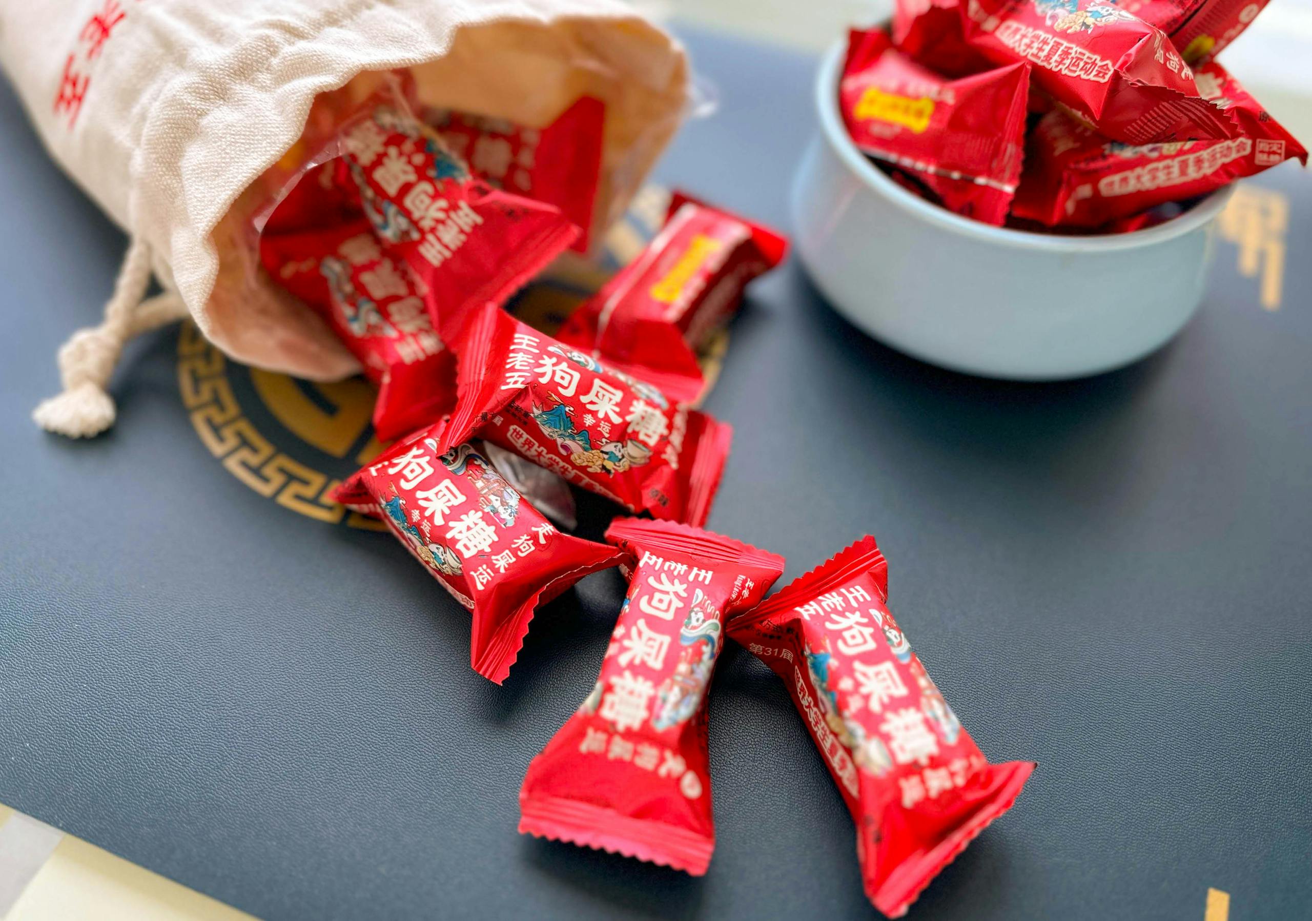 Top view of red-wrapped candies spilling from a bag on a black surface, showcasing vibrant packaging.
