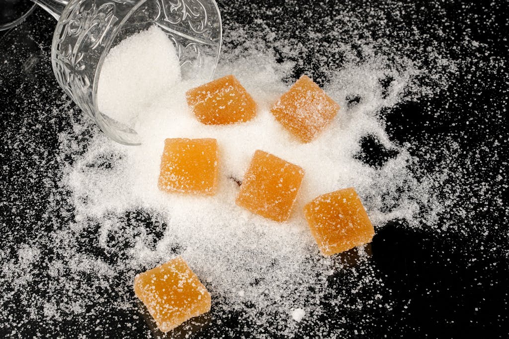 Top view of sugar cubes scattered from a glass jar onto a black surface with granulated sugar.