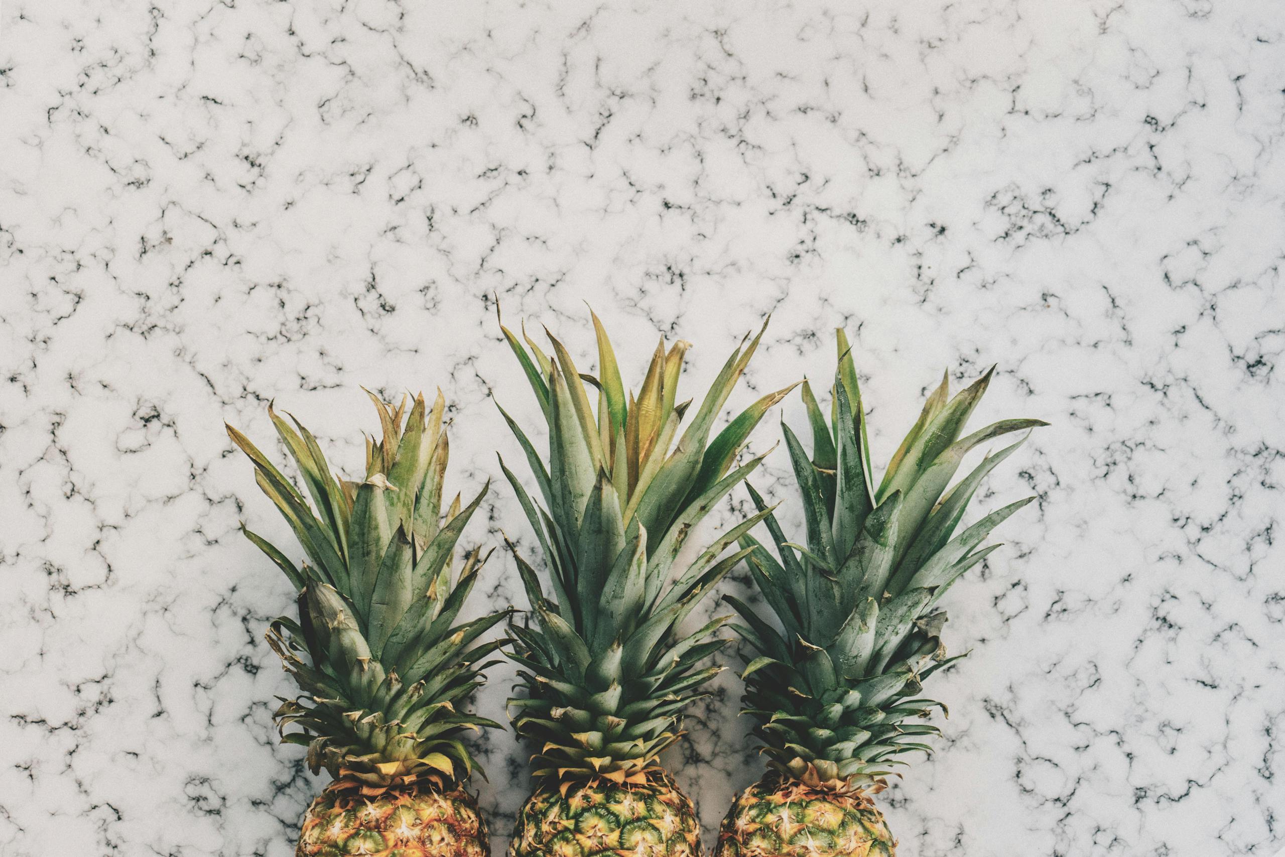 Top view of three ripe pineapples on a stylish marble surface, perfect for a tropical vibe.