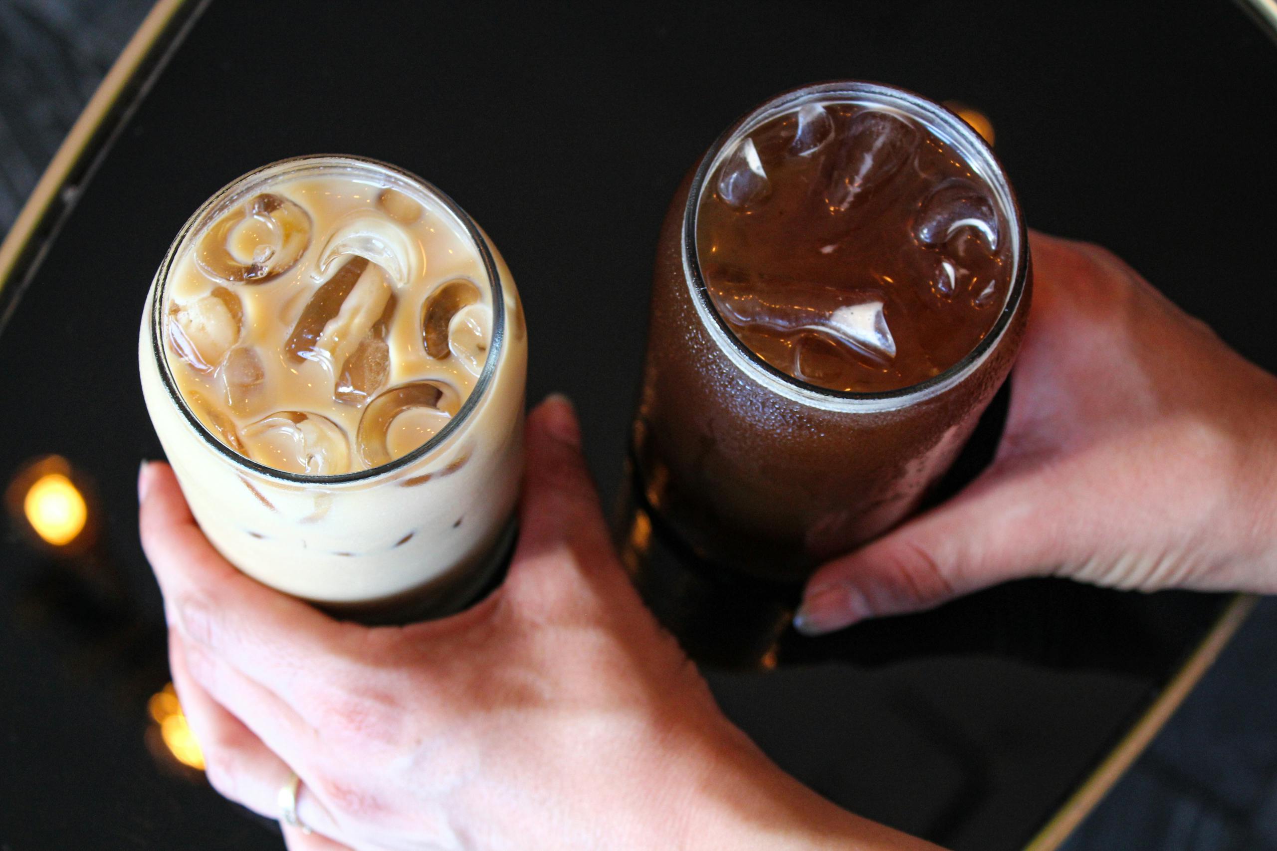 Top view of two iced beverages being held over a reflective black surface - perfect for a refreshing break.
