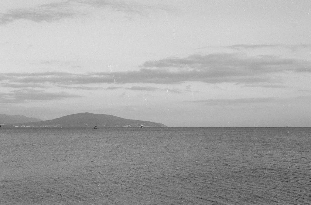 Tranquil black and white seascape view of the Novorossiysk coastline in Russia, showcasing calm seas and distant hills.