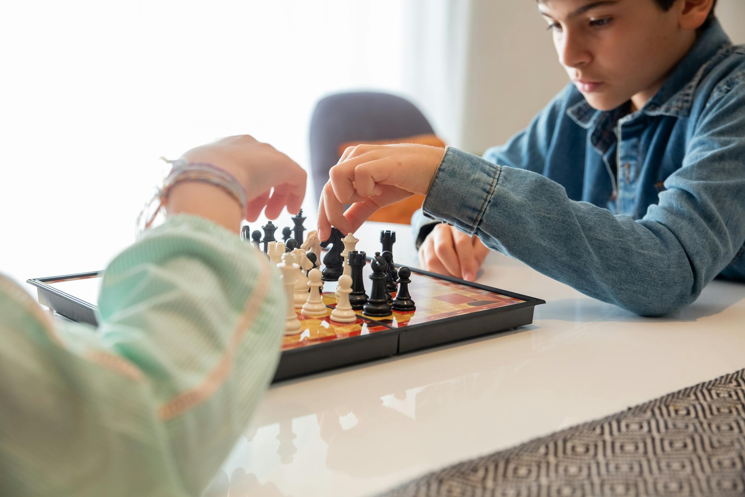 Two children playing chess, focusing on game strategy indoors. Ideal for depicting concentration and leisure.