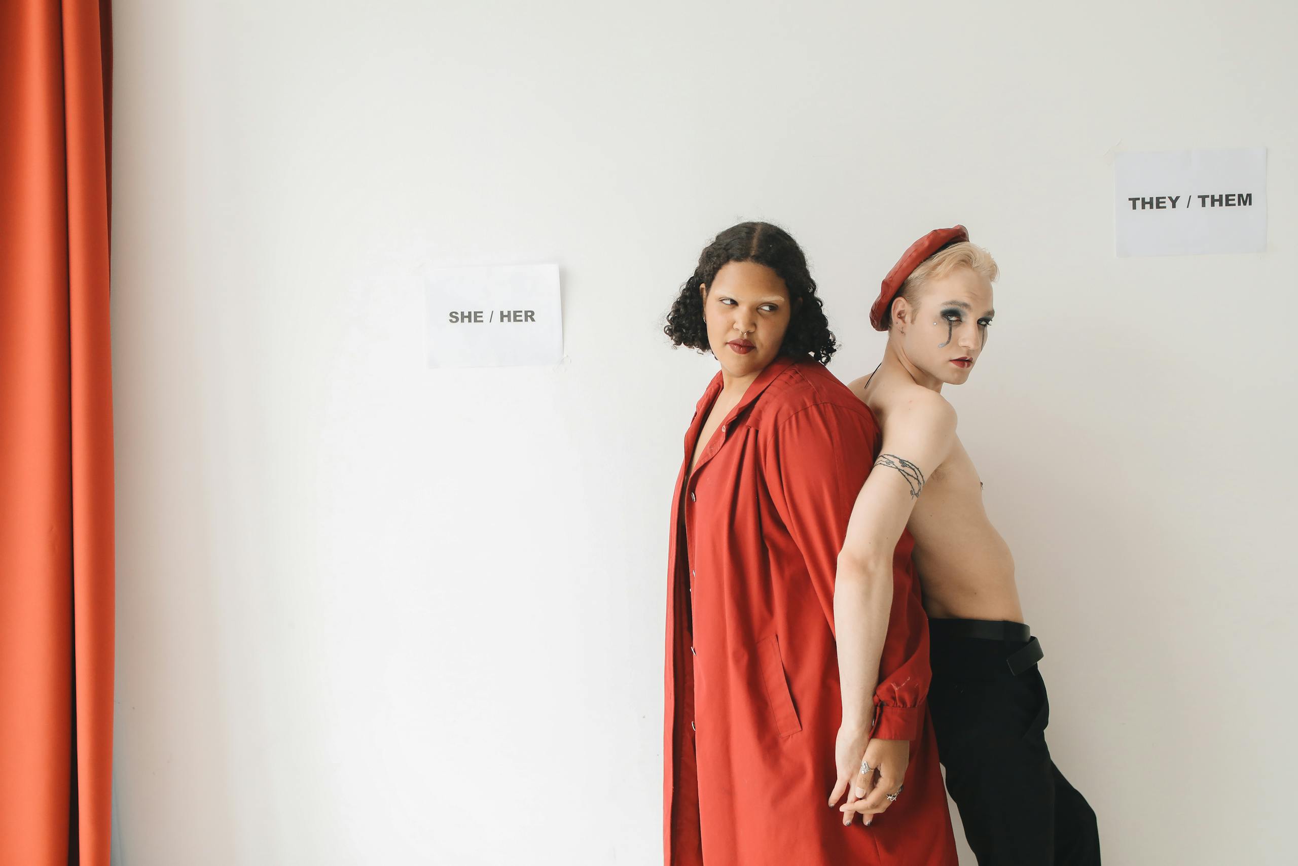 Two individuals expressing gender diversity with unique fashion choices against a neutral background.