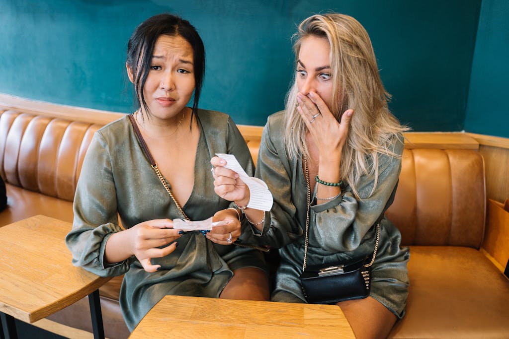 Two women express surprise while reviewing a restaurant bill in a casual setting.