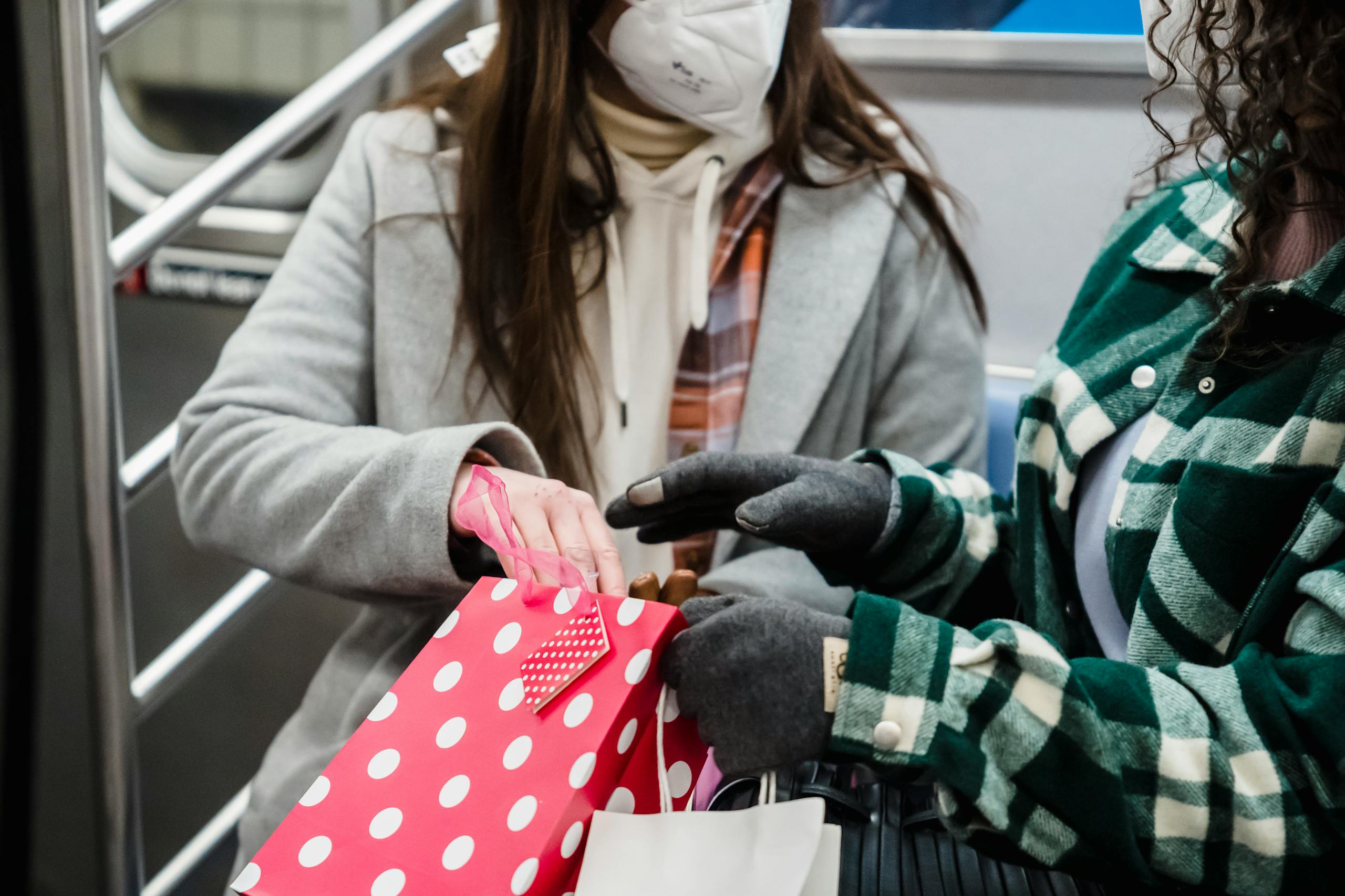 Two women in masks sharing shopping bags on a subway, reflecting the new normal lifestyle.