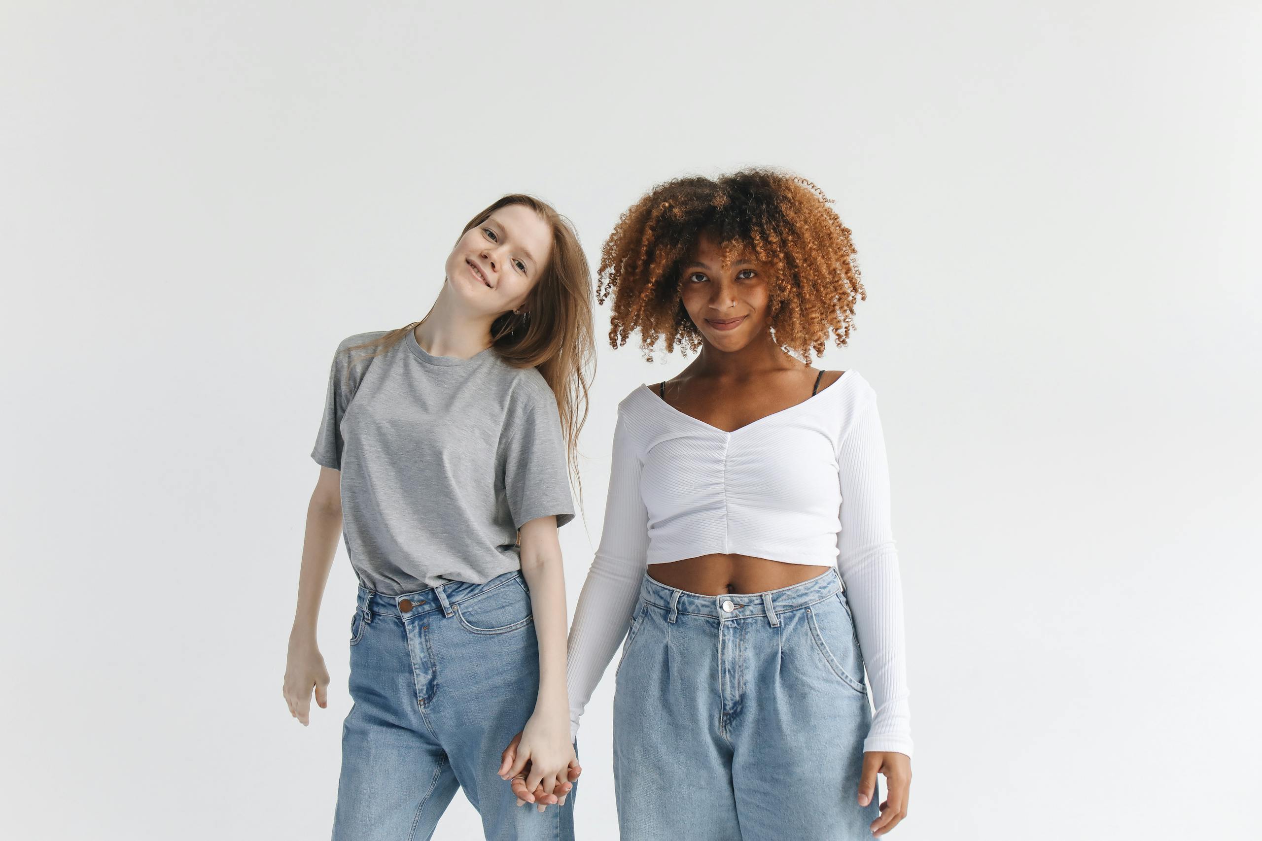 Two women with diverse backgrounds smiling and holding hands, showcasing friendship.