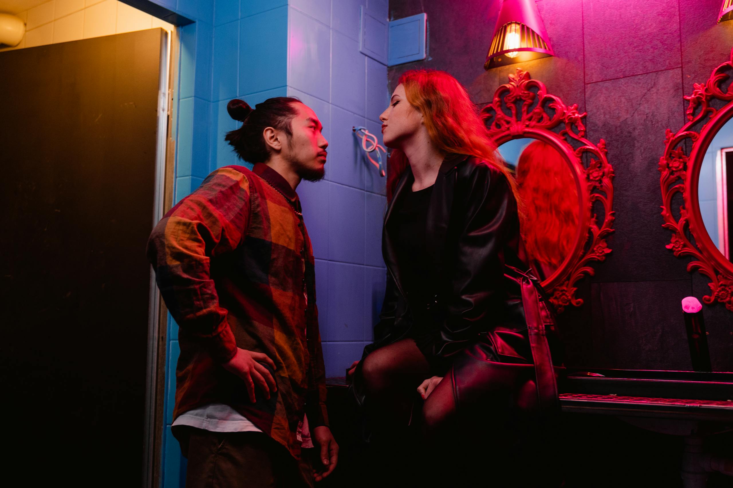 Two young adults in a stylish nightclub setting, illuminated by colorful lights.